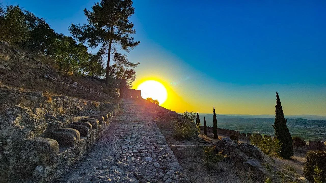 Sunset over ancient ruins with stone pathway and cypress trees