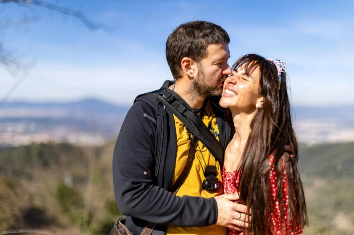 A couple sharing a kiss outdoors, with a scenic landscape in the background.