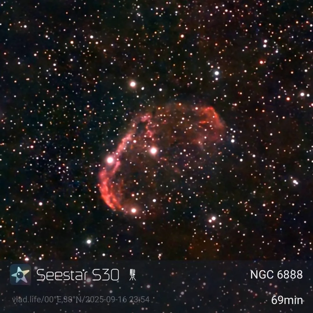 A colorful deep space image showing a nebula with red and pink hues amidst a field of stars.