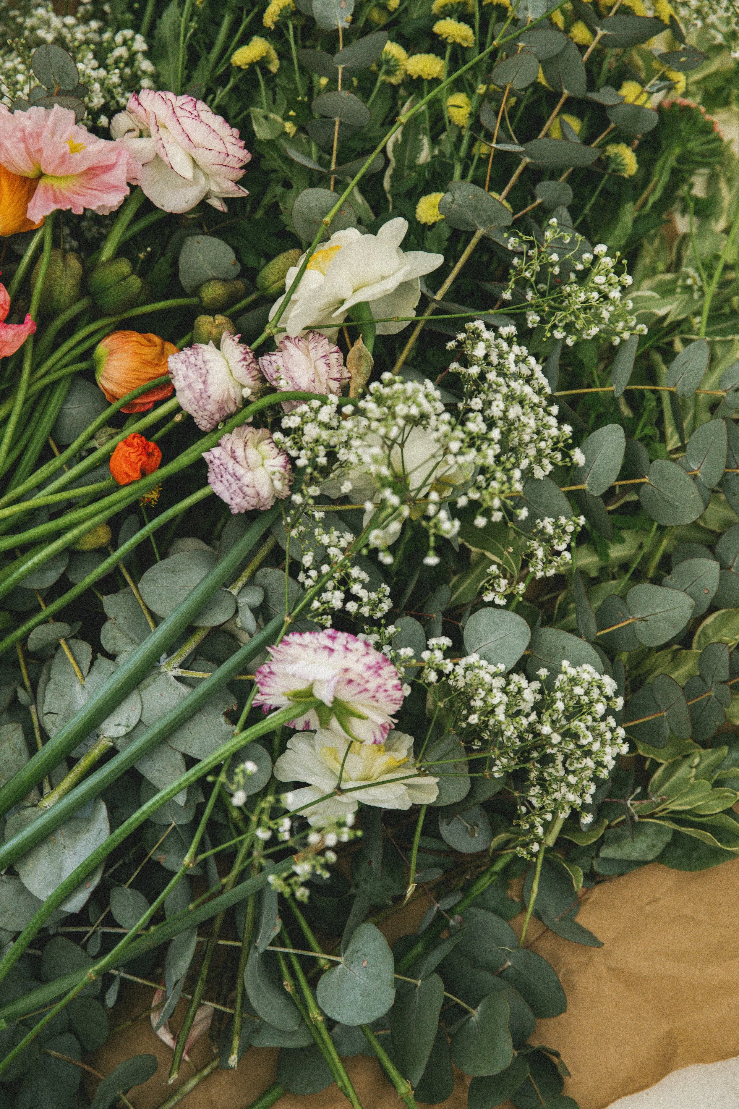 Arrangement of various colorful flowers including white, pink, orange, and yellow with green foliage around.