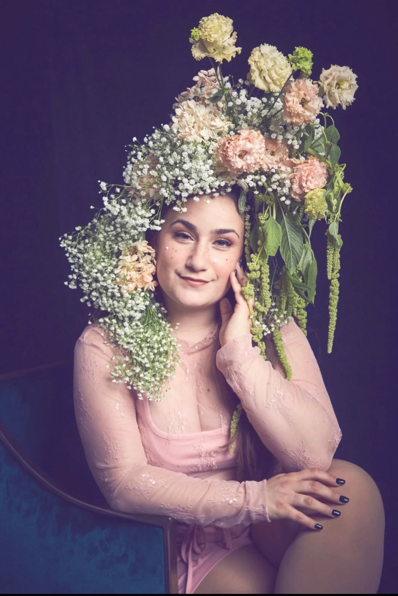 Cat Rojo posed with her hand on her face wearing an elaborate floral headpiece with draping greenery at the Solstice Soirée for The Old Globe in San Diego