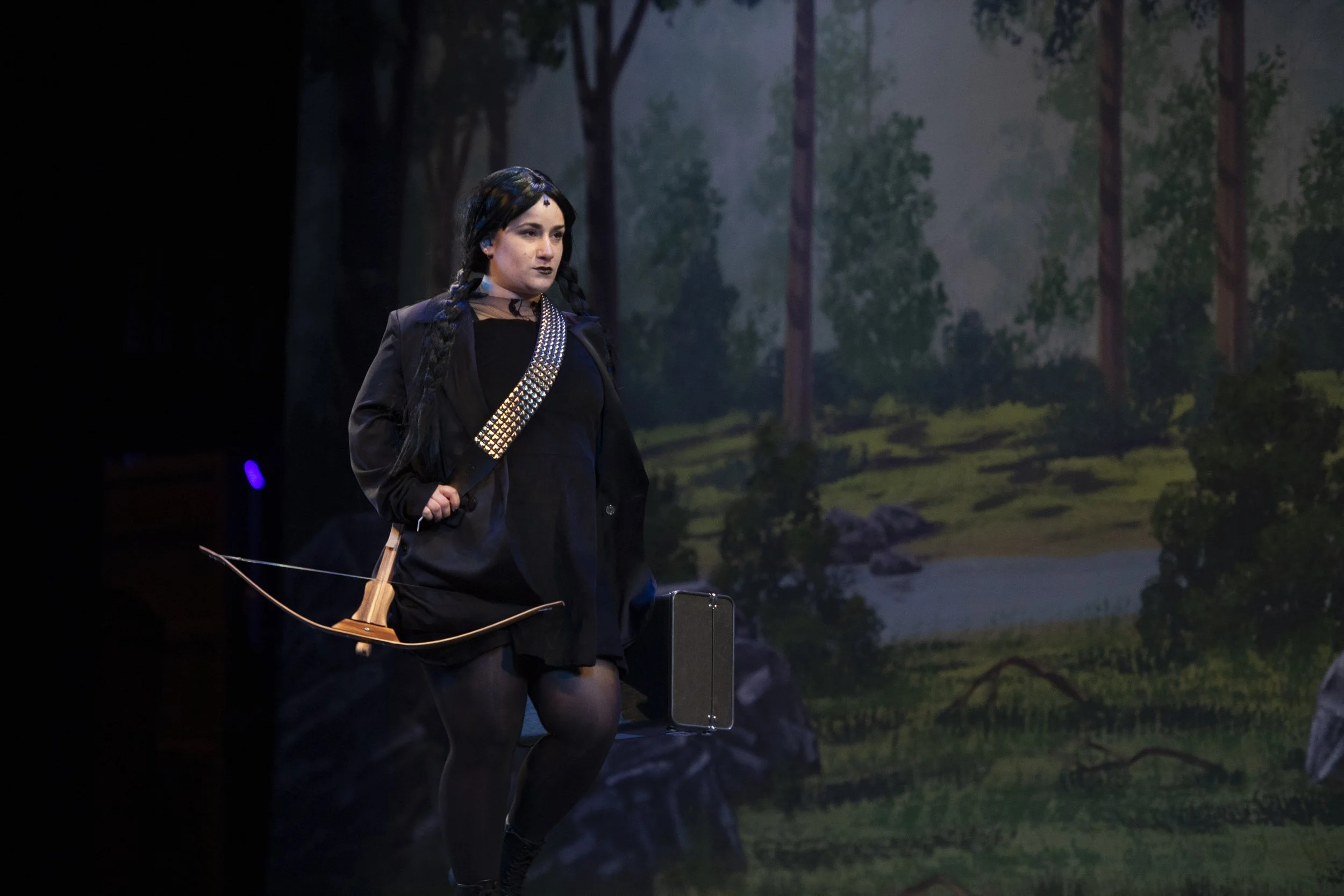 Cat Rojo as Wednesday Addams charging forward with a bow and arrow