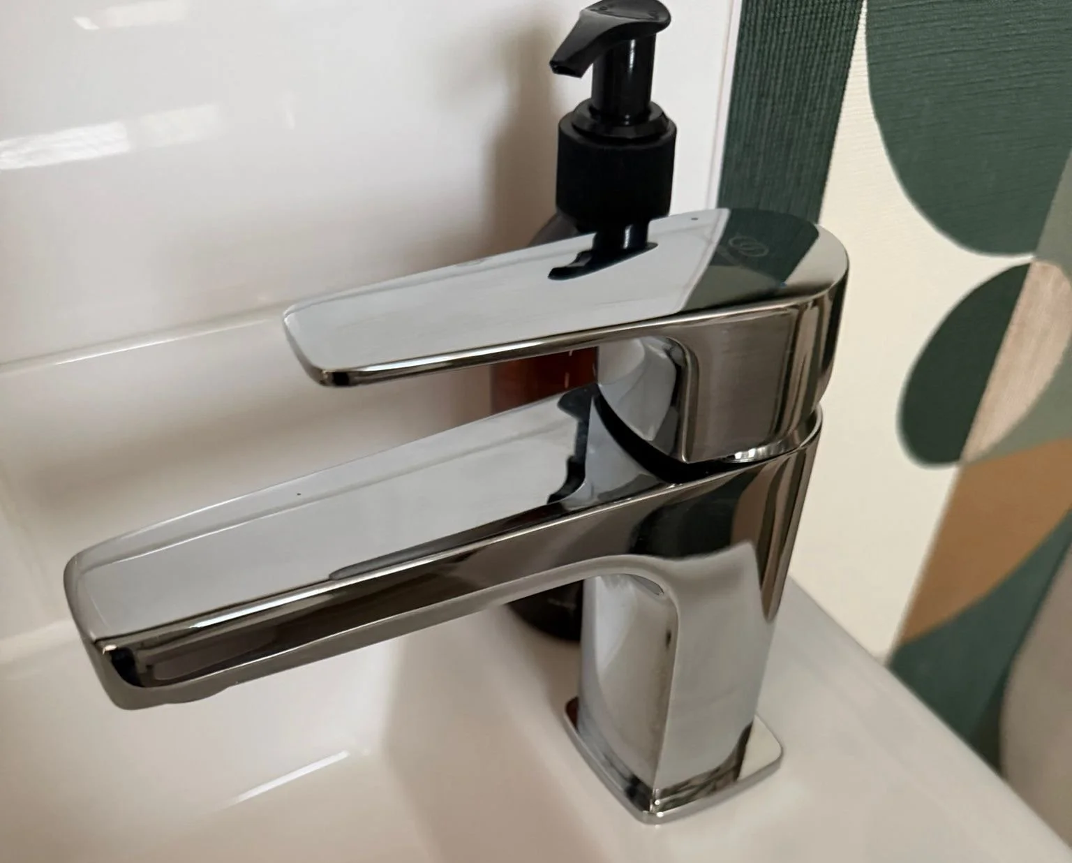 A modern chrome faucet with a black soap dispenser on a white bathroom sink.