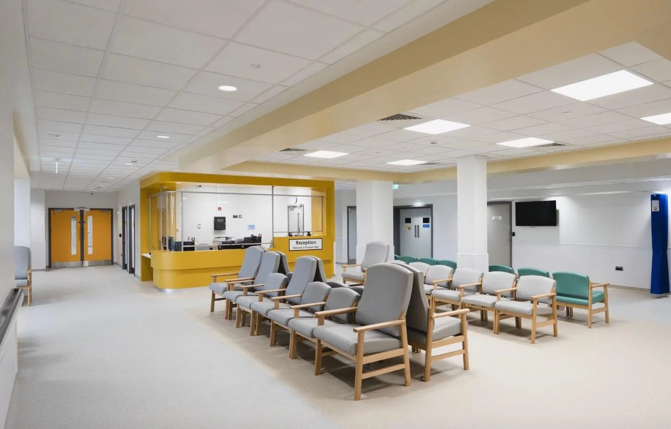 Hospital waiting room with multiple chairs, a reception desk, and a television on the wall.