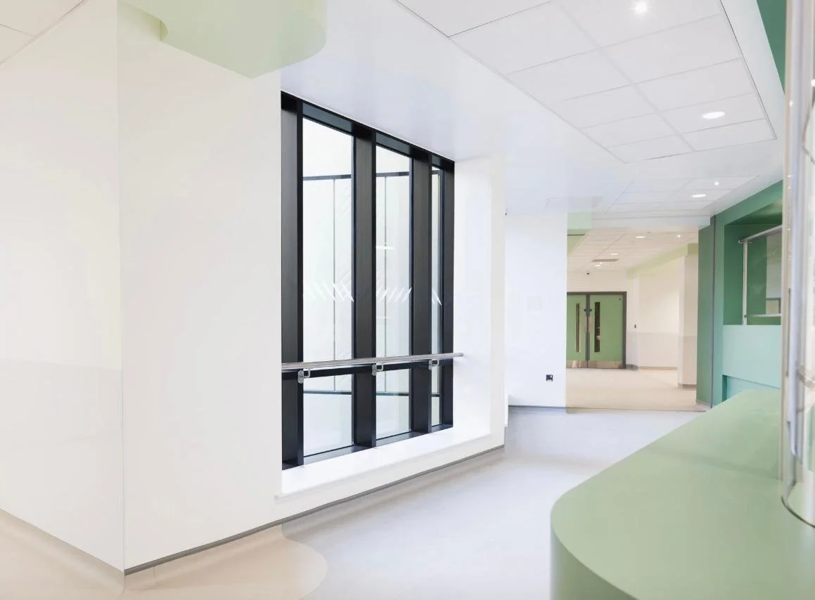Bright, modern interior with large black-framed windows, white and green walls, and a curved green counter.
