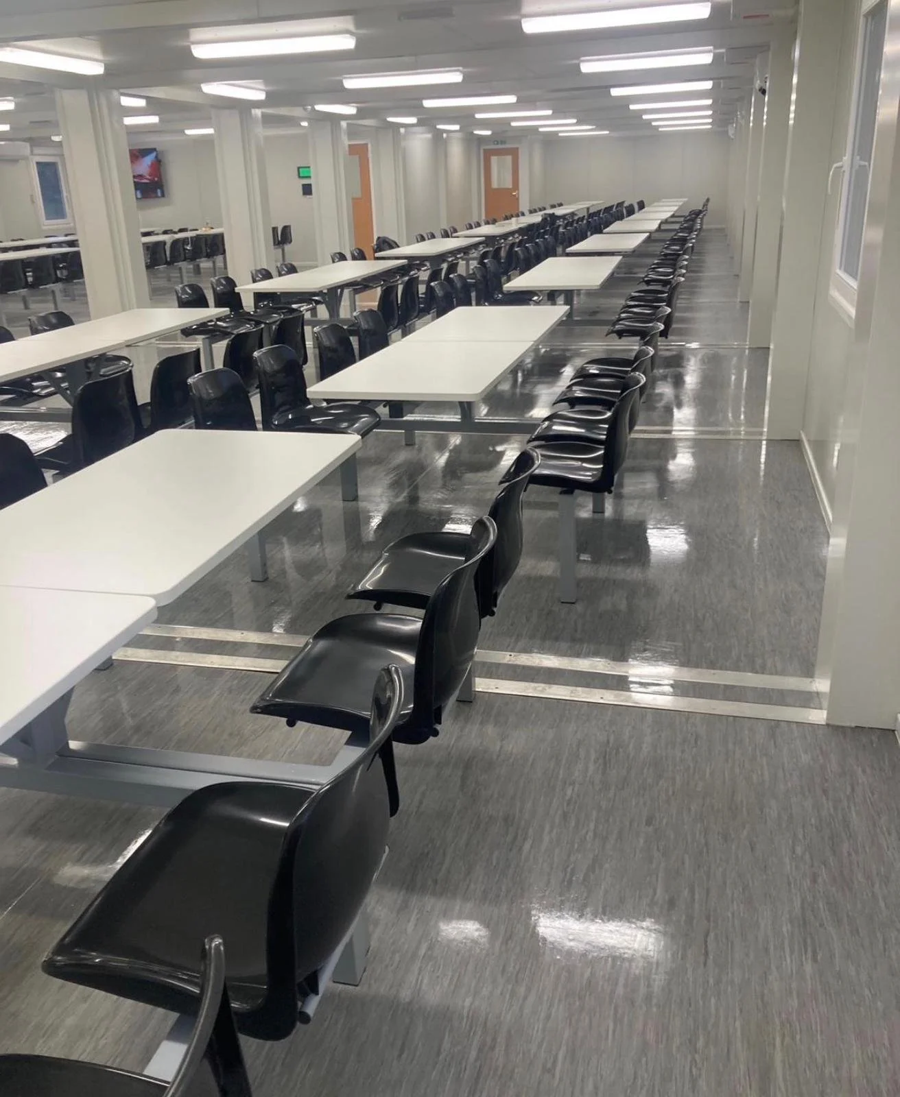 Empty cafeteria with black chairs and white tables arranged neatly in rows.