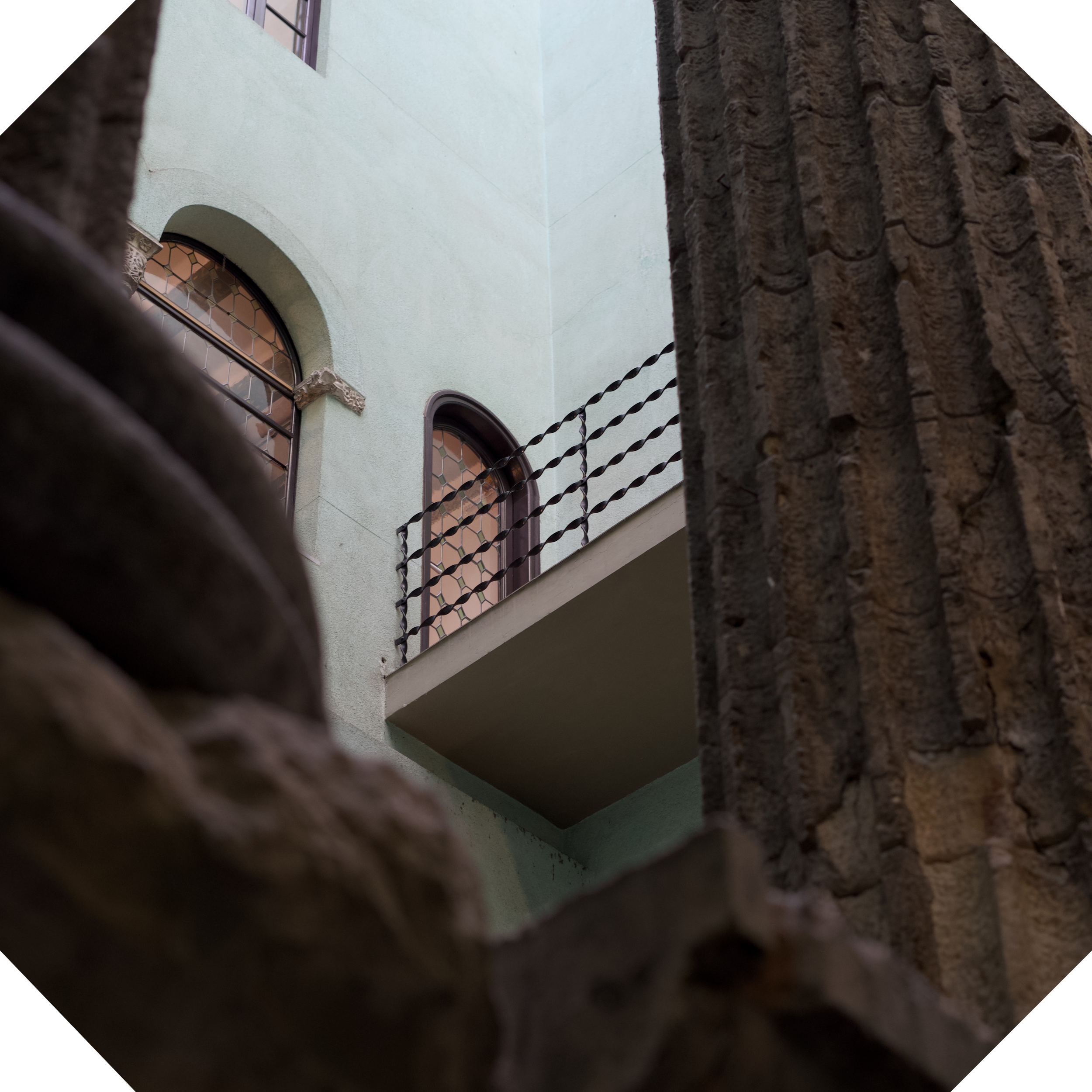 Vista desde abajo de un edificio con ventanas arqueadas y rejas de hierro, rodeado por una estructura de piedra con detalles de madera y metal.