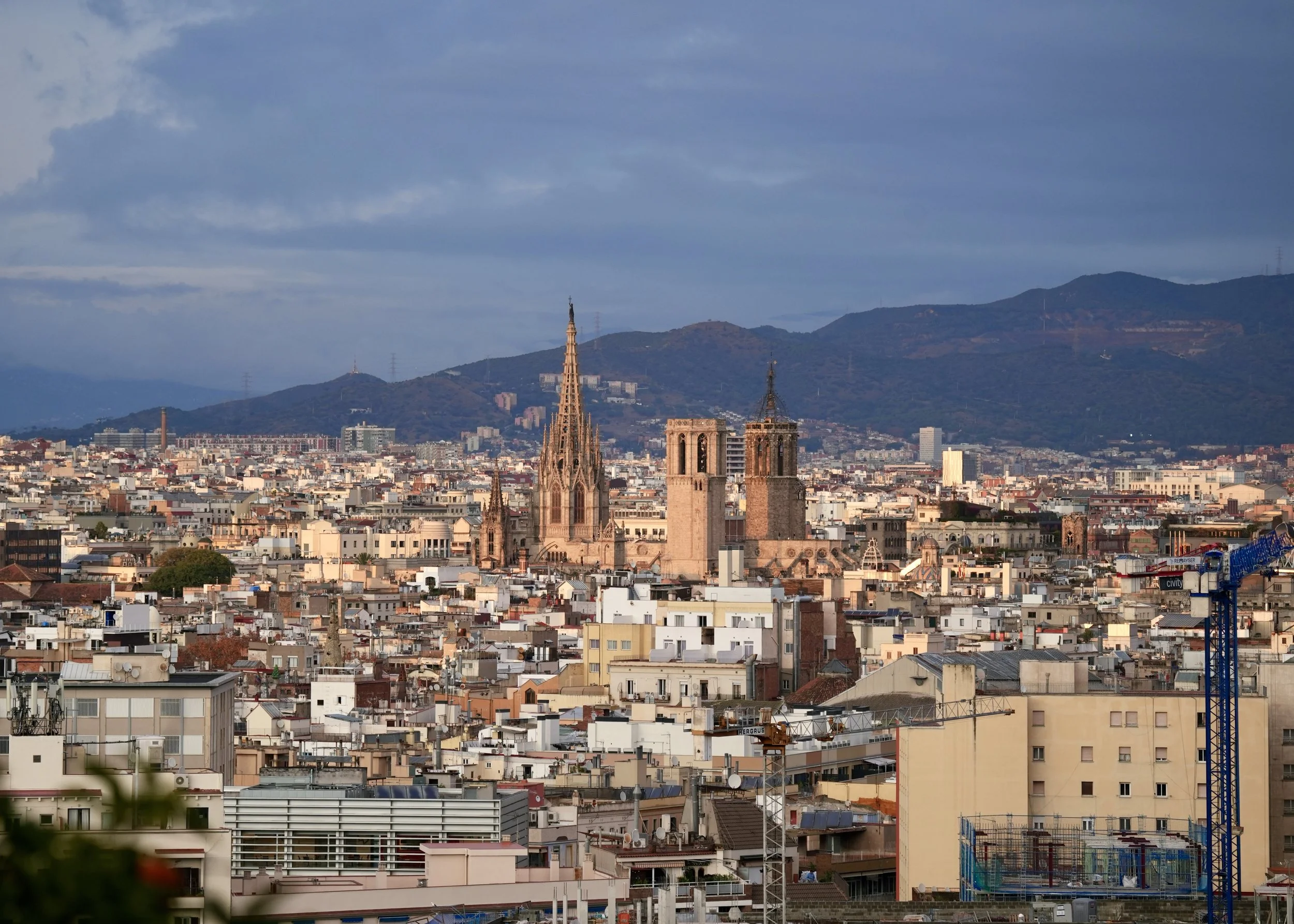 Vista panorámica de la ciudad con catedrales antiguas en primer plano y montañas en el fondo, cielo nublado.