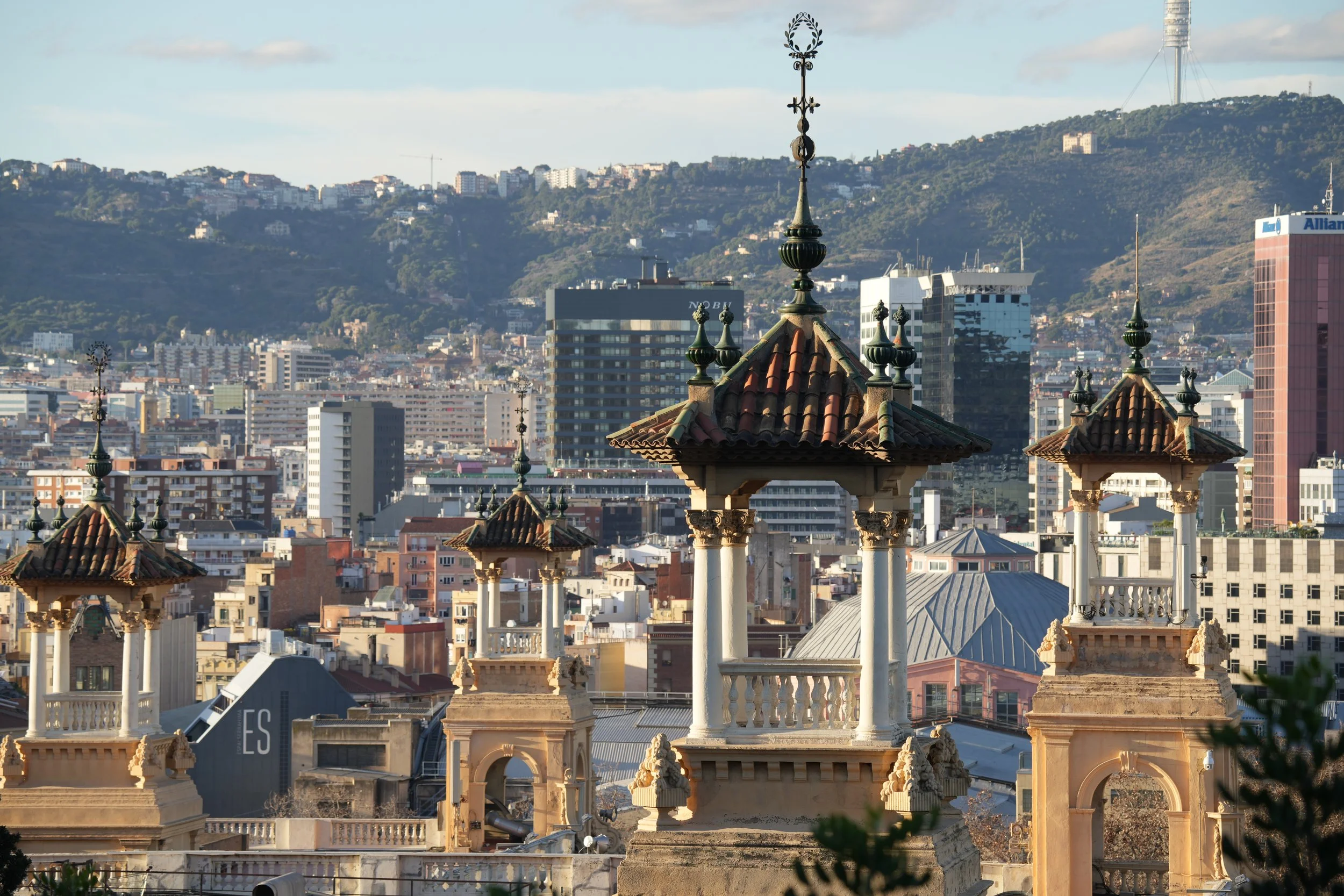 Vista urbana con techos de terracota y detalles en piedra, y un fondo de colinas verdes con edificios modernos.