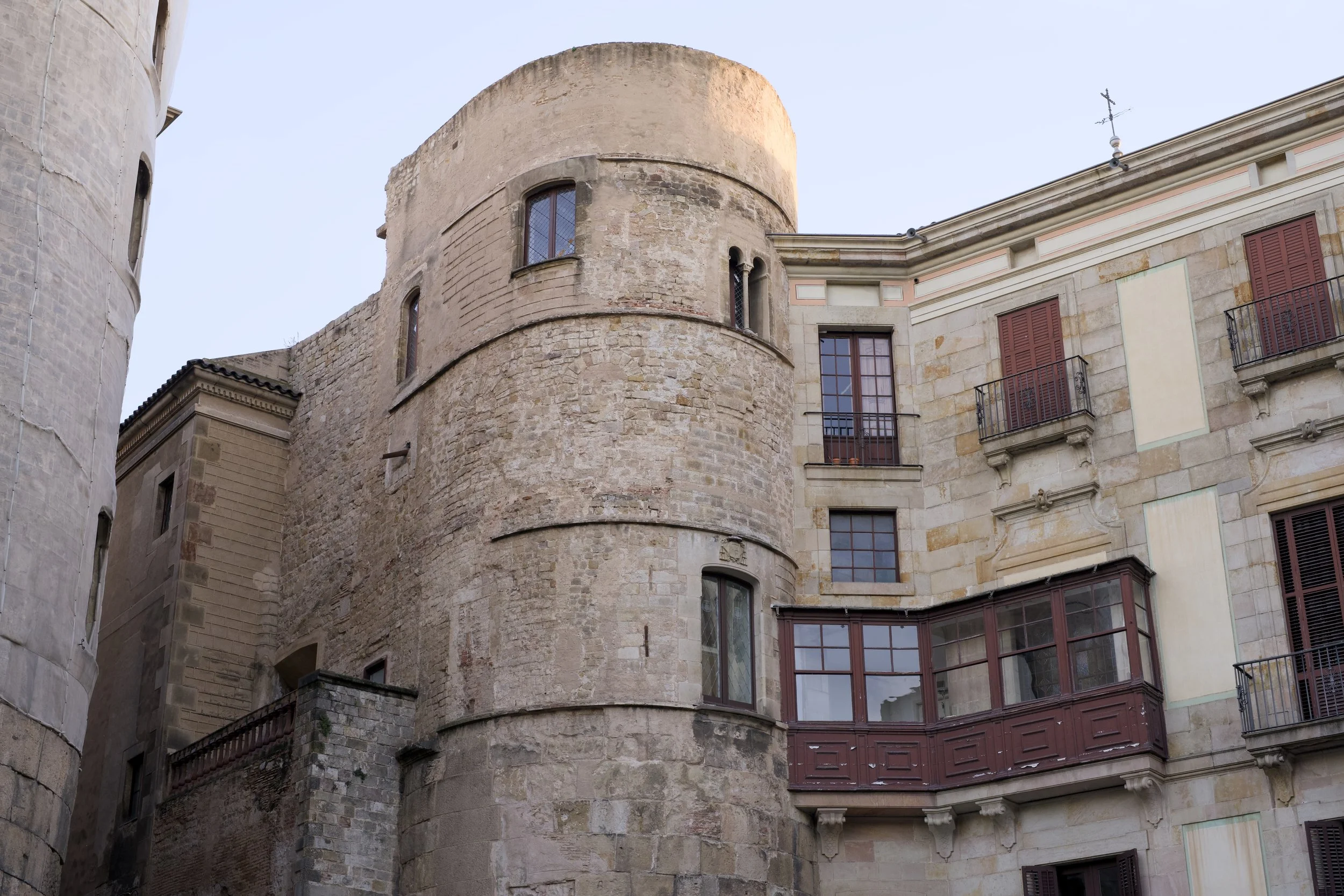 Edificio histórico de piedra con varias ventanas, balcones y una estructura curva en la parte central, en un entorno urbano.