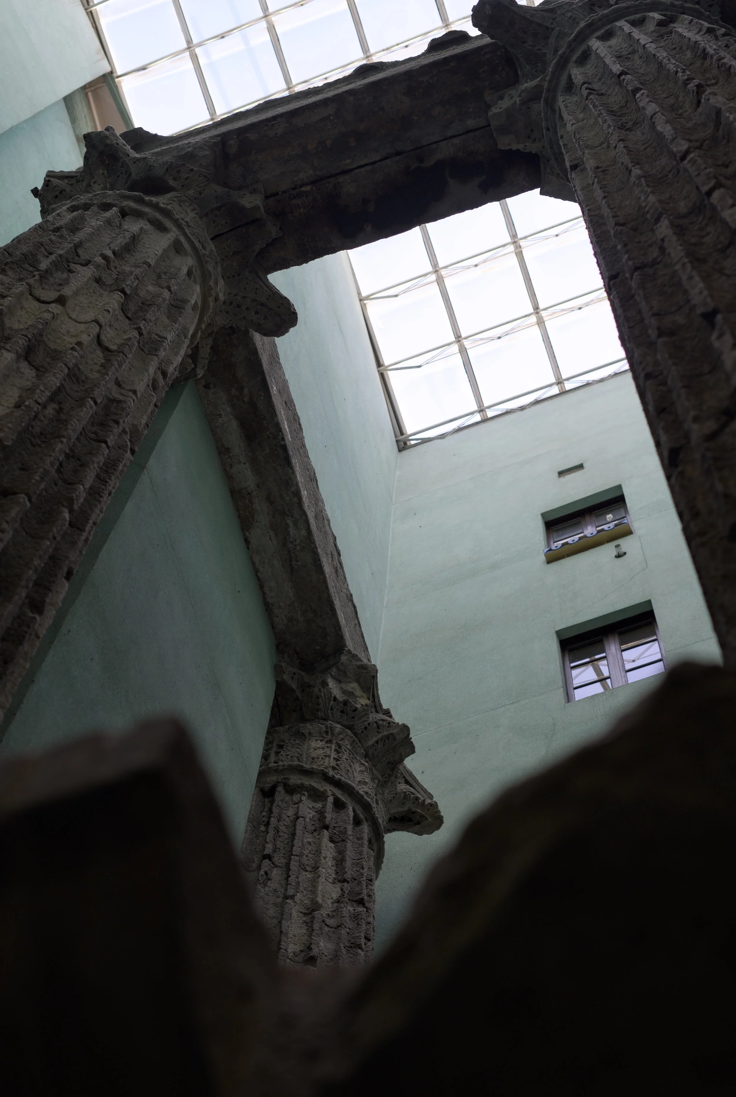 Vista desde abajo de columnas con detalles tallados en piedra, en un espacio interior con ventanas y luz natural