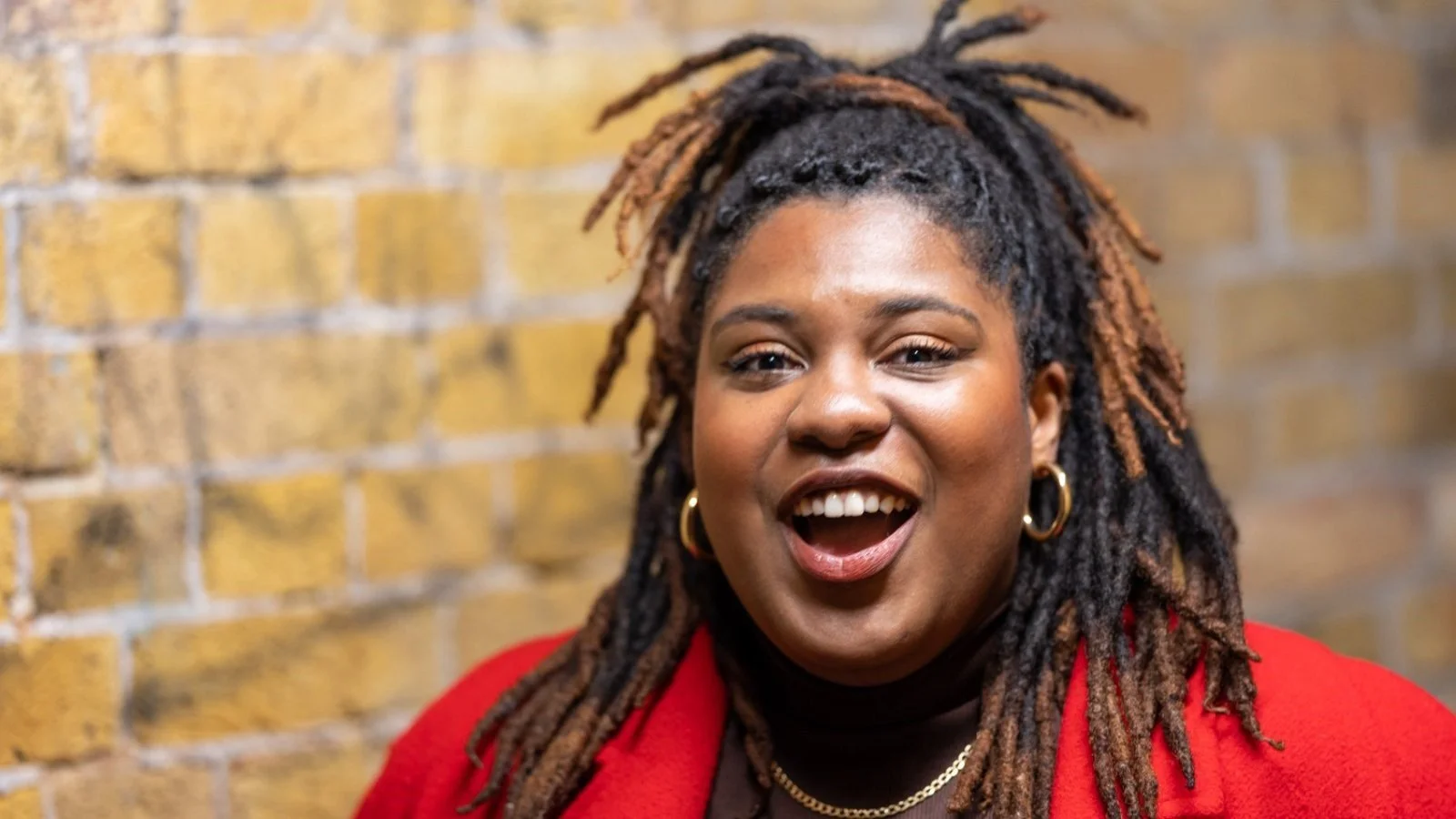 Photo credit: Steve Cross. Rachel Honeyghan-Williams smiles against the backdrop of a brick wall.