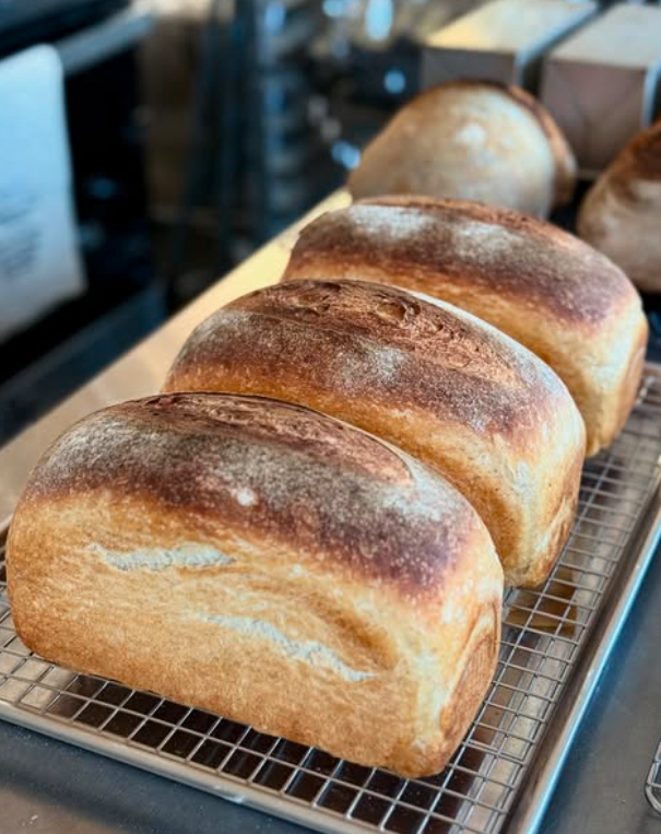 Southeast Sourdough's freshly baked loaves of bread cooling on a wire rack in a bakery.