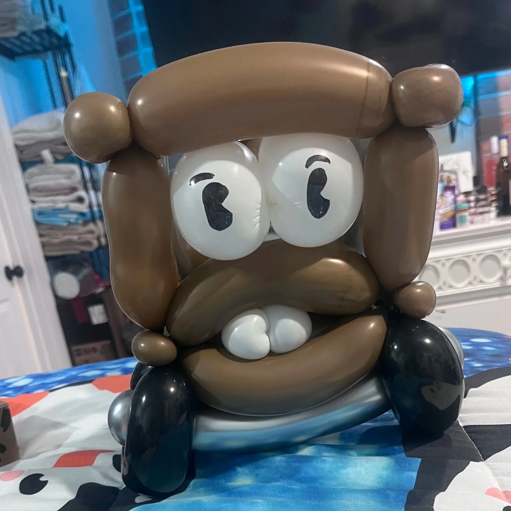 Balloon sculpture of a cartoon character with large eyes and a brown hat and beard, sitting cross-legged on a table.