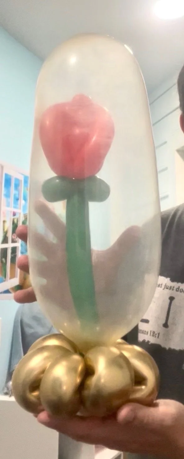 A person holding a glass decorative sculpture of a pink flower with a green stem and gold base.