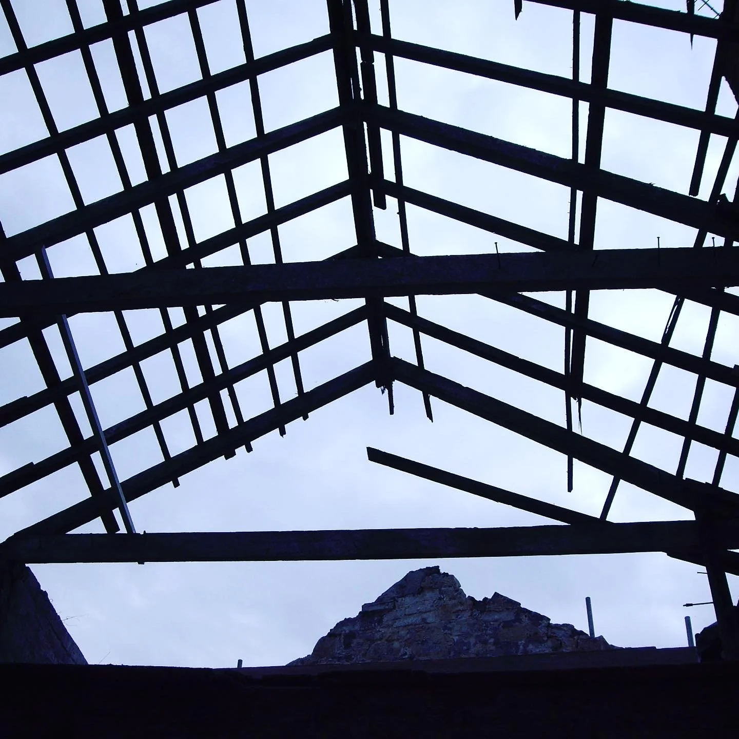 View of a building's roof structure under construction, showing exposed wooden beams and framework against a cloudy sky.