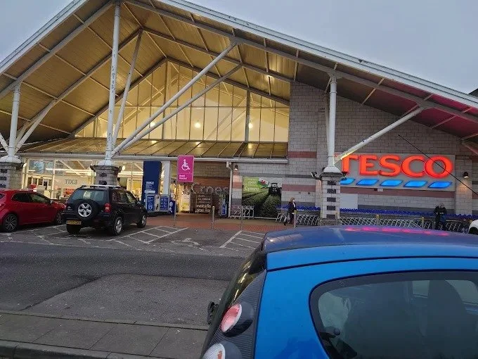 Exterior of a Tesco supermarket, Penarth, with a parking lot and several cars parked.