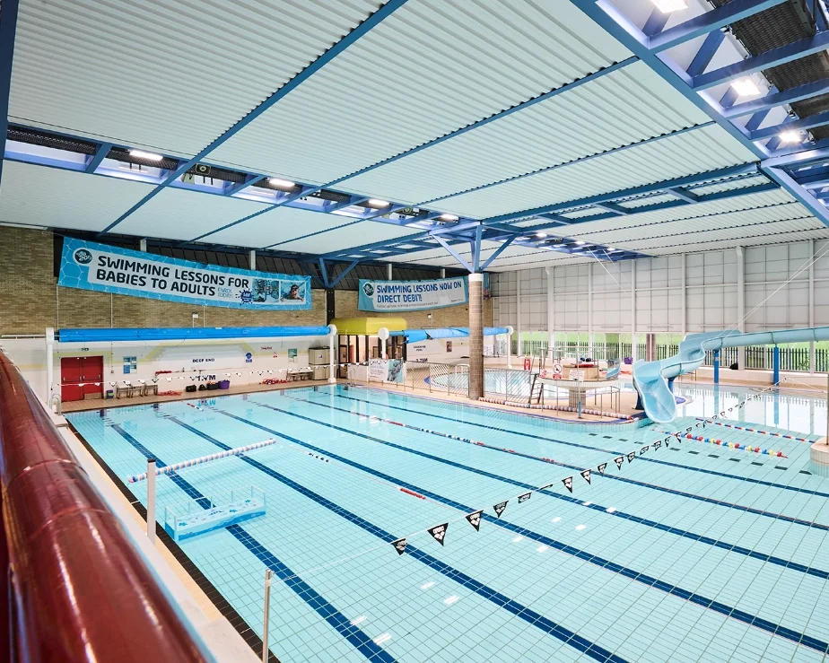 Penarth Leisure Centre, Indoor swimming pool with lanes, a water slide, and banners advertising swimming lessons for all ages.