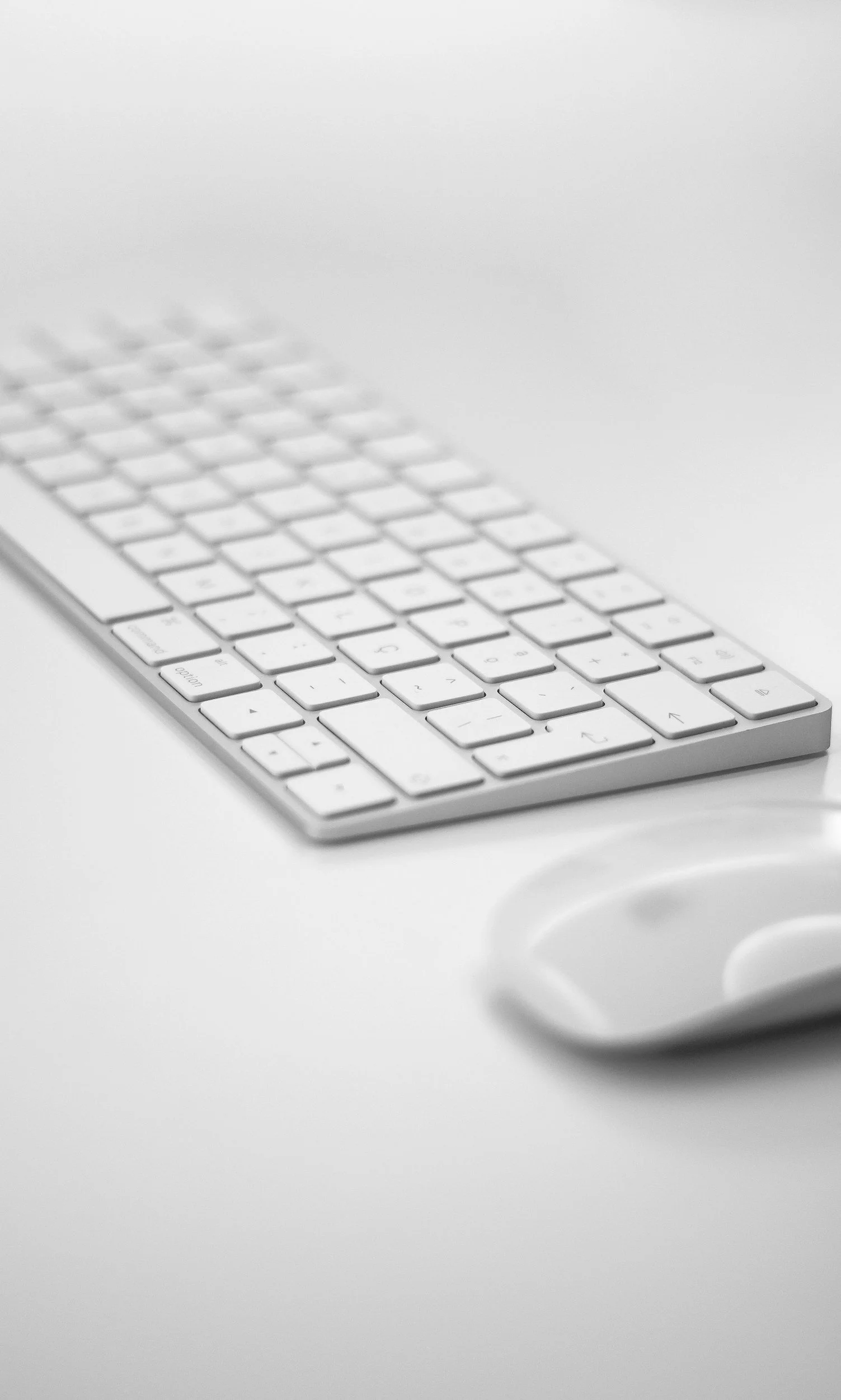 A white wireless keyboard and a white computer mouse on a white surface.