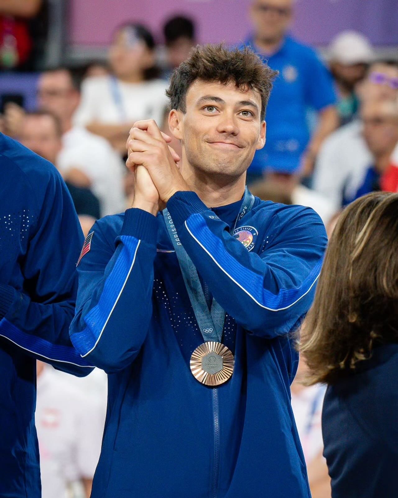 Micah Ma'a in a blue sports jacket with a medal around his neck, smiling, at an award ceremony or celebration event.