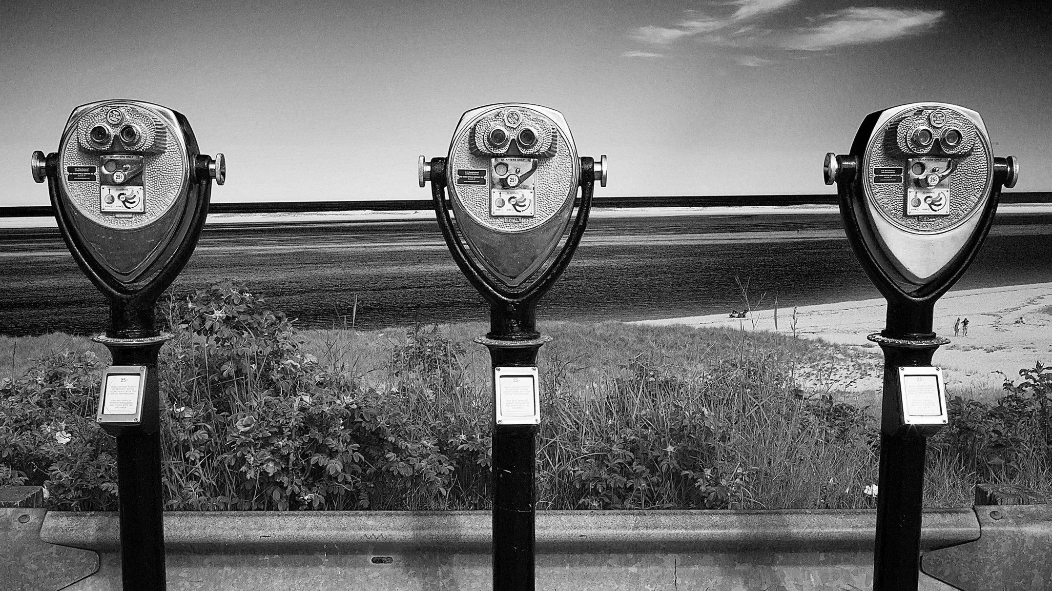 Three coin-operated tower viewers at Chatham Light, Cape Cod, overlooking the Atlantic Ocean and beach with a few people walking.