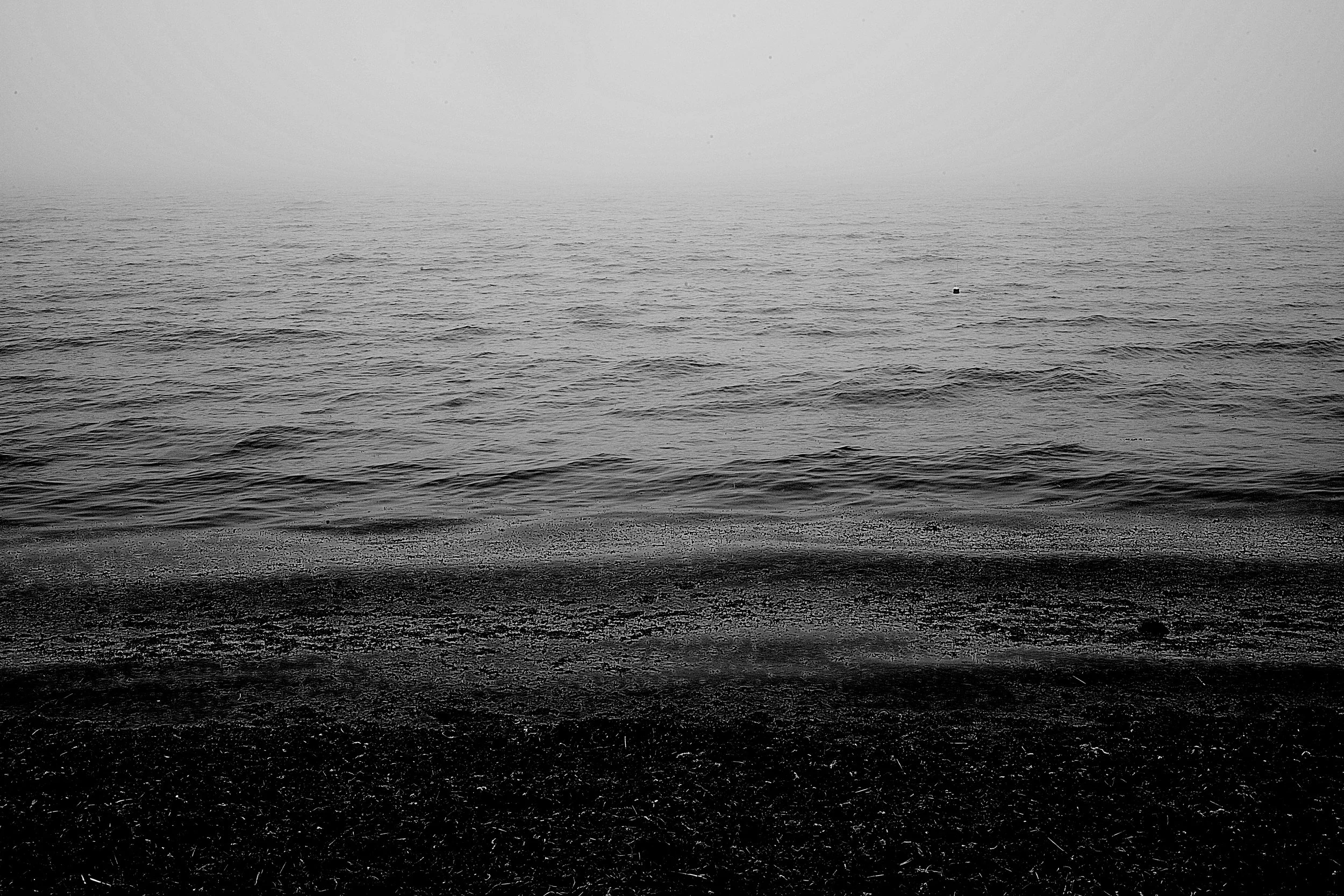 Black and white photograph of a moody ocean with seaweed in the waves out on Cockle Cove South Chatham