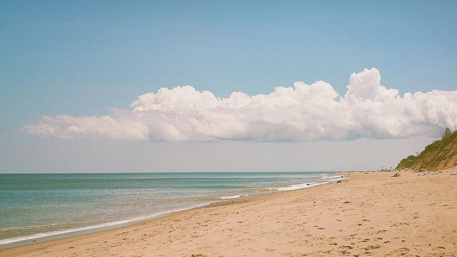 A sandy beach with calm ocean water and a partly cloudy sky out on Nauset Beach Cape Cod, MA.