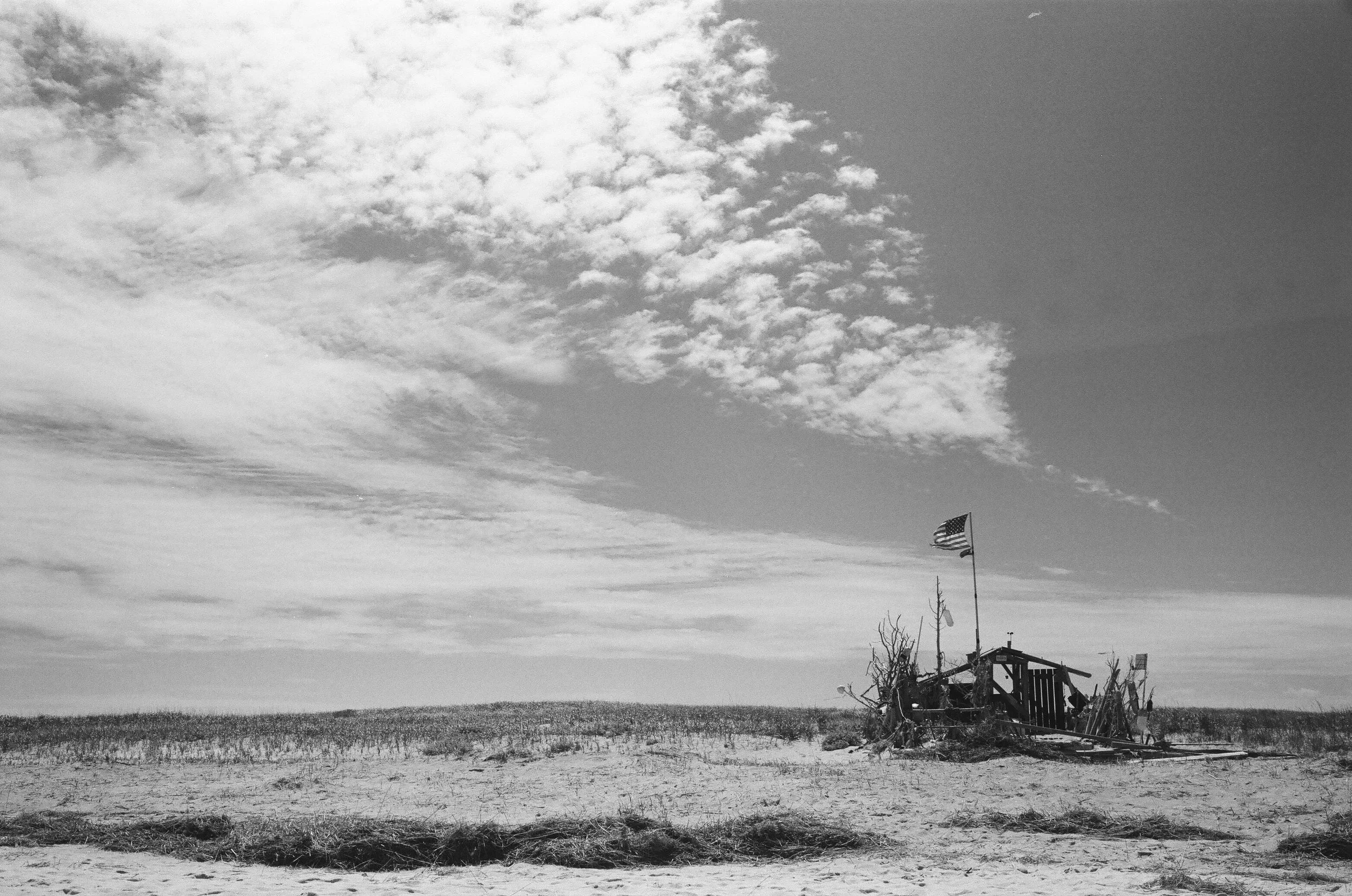 Black and White photograph of the structure on Chatham Light Beach with the Stars and Stripes flag flying