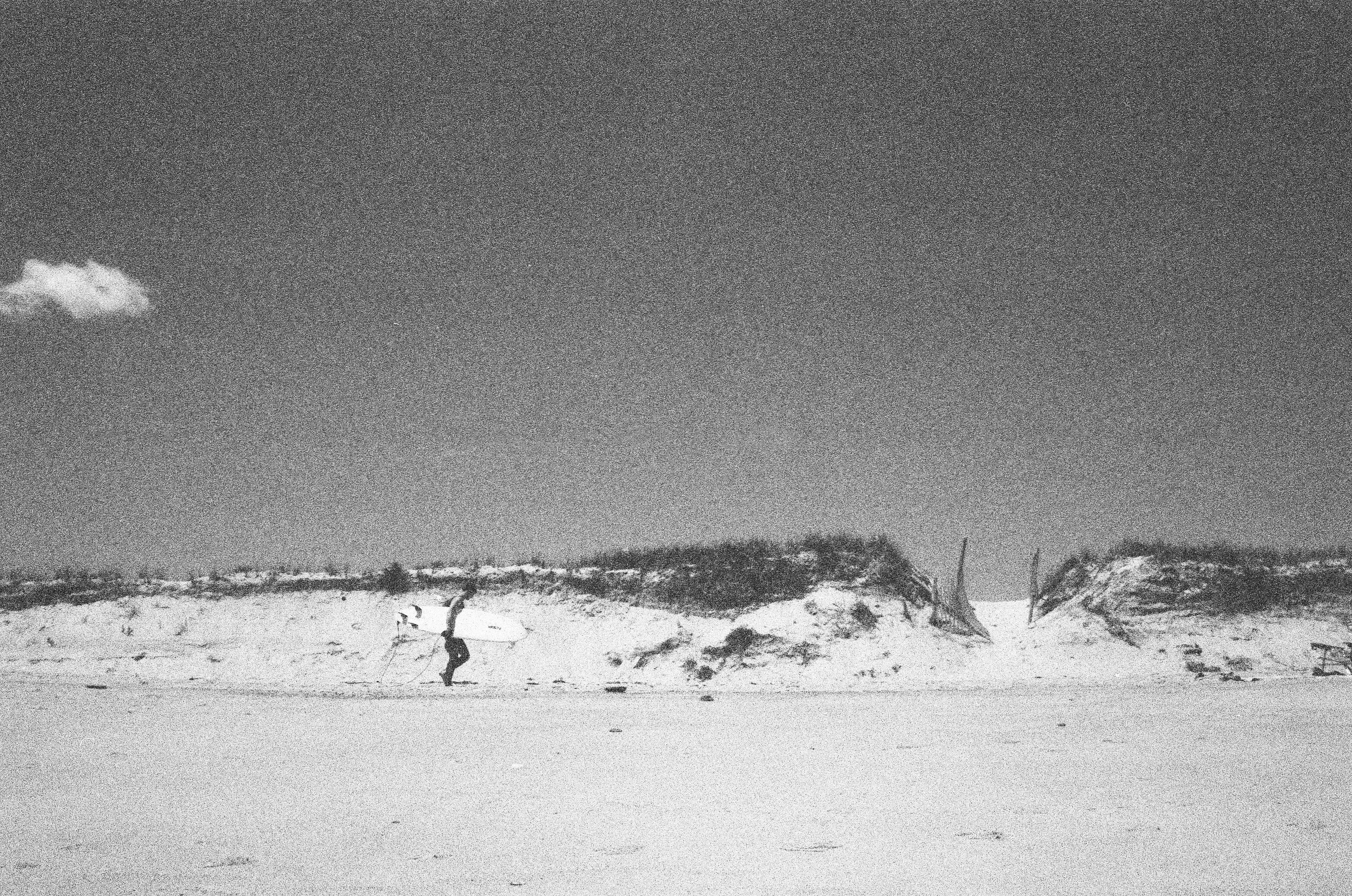 Grainy black and white photograph of a surfer returning from a day out on Nauset Beach surfing