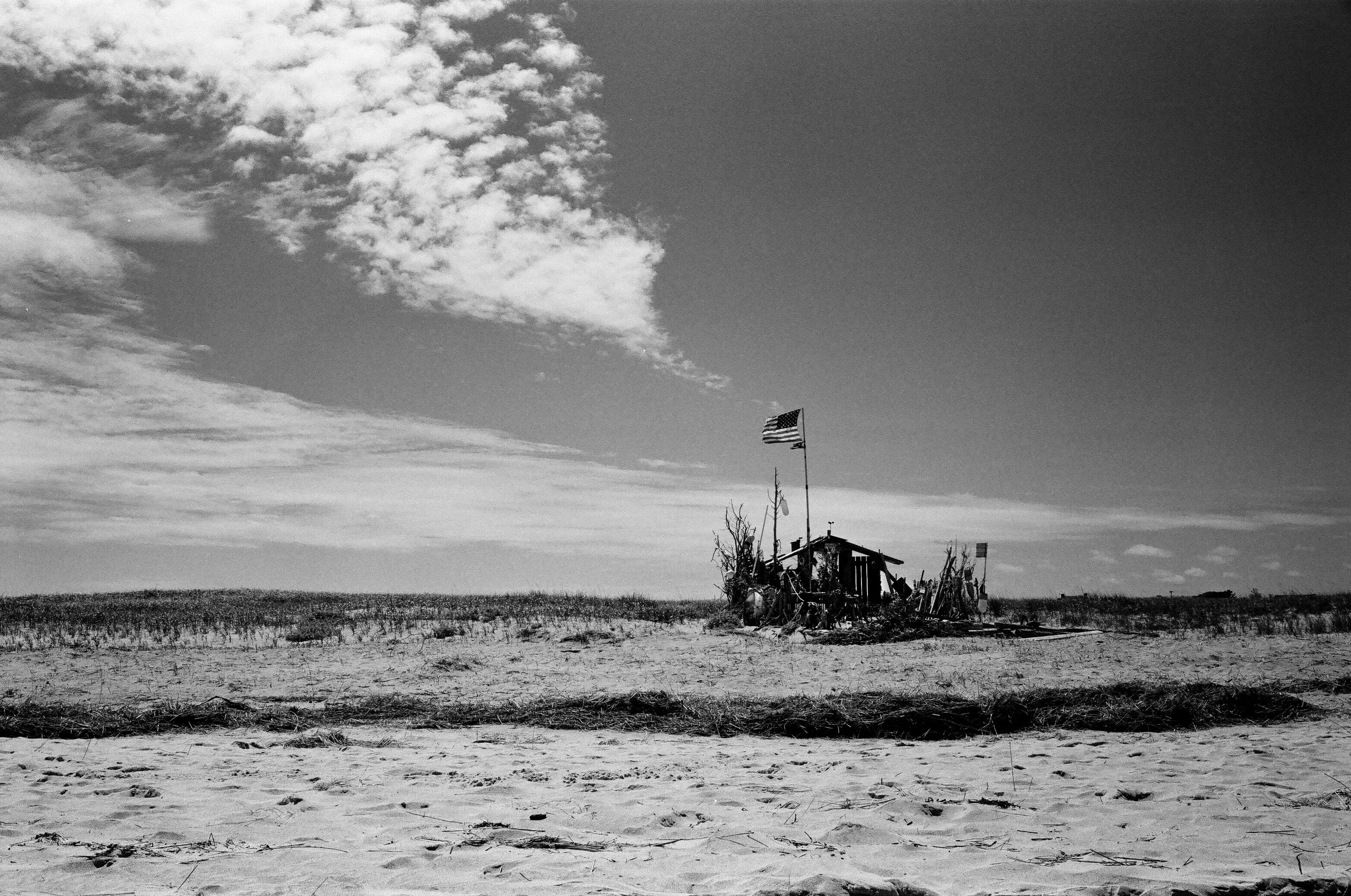 Black and White photograph of the building on Chatham light Beach with the American flag flying and clouds in the sky