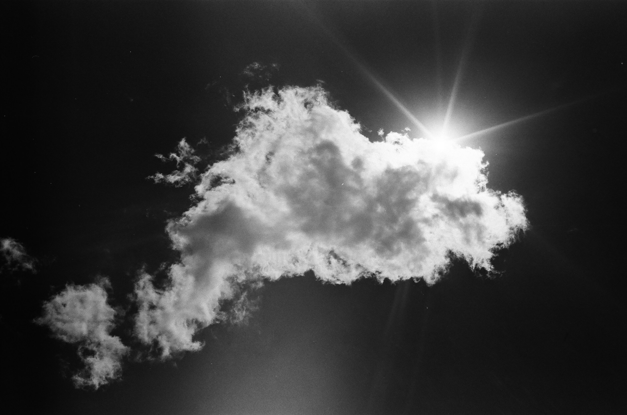 Black and white photograph of a cloud and the sun's rays shining out from behind the cloud