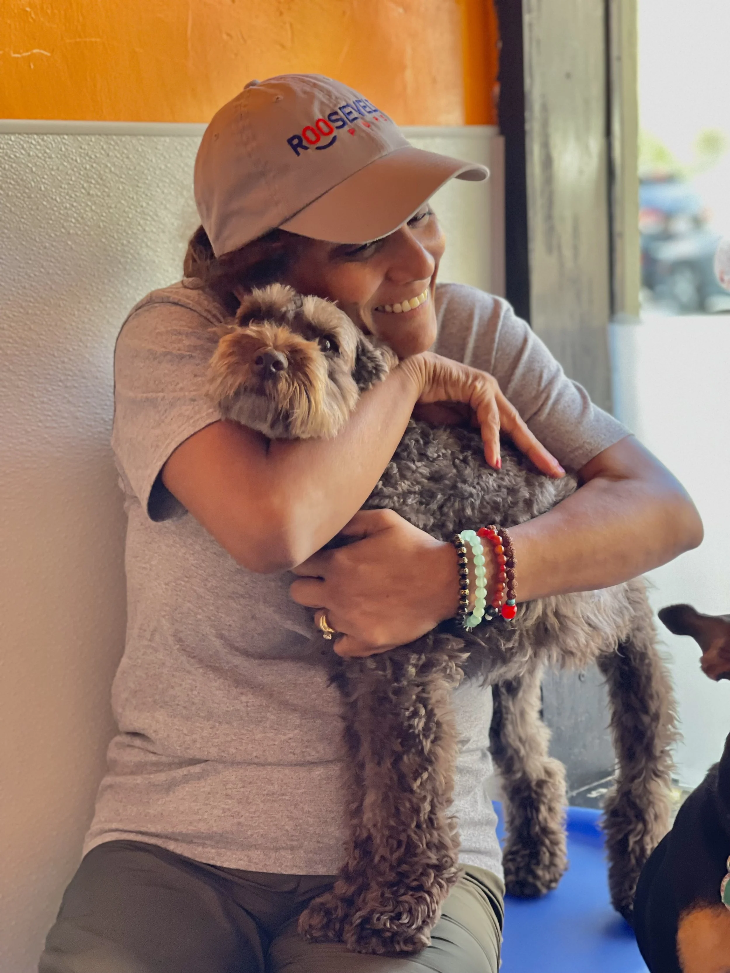 A woman wearing a white cap hugging a fluffy brown and gray dog in a cozy indoor setting.