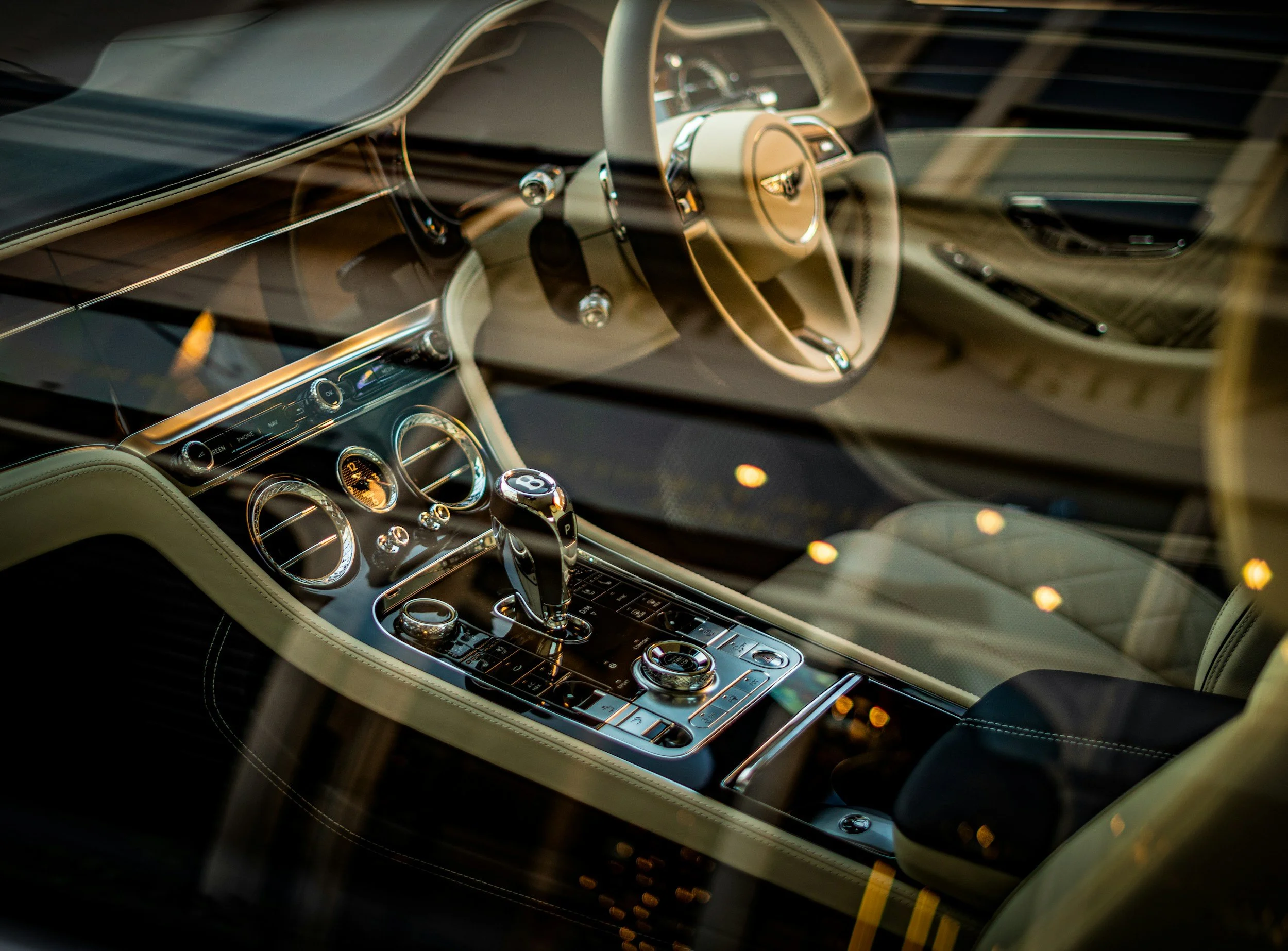 Interior of a luxury sports car showing the steering wheel, dashboard, and center console with gear shift and control knobs, viewed through the windshield.