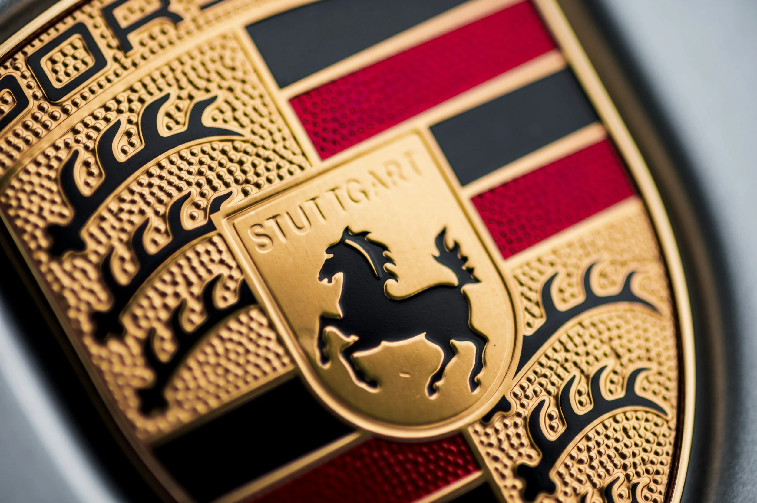 Close-up of a Porsche badge featuring a black horse on a yellow shield with red and black stripes, and the text 'STUTTGART' above the horse.