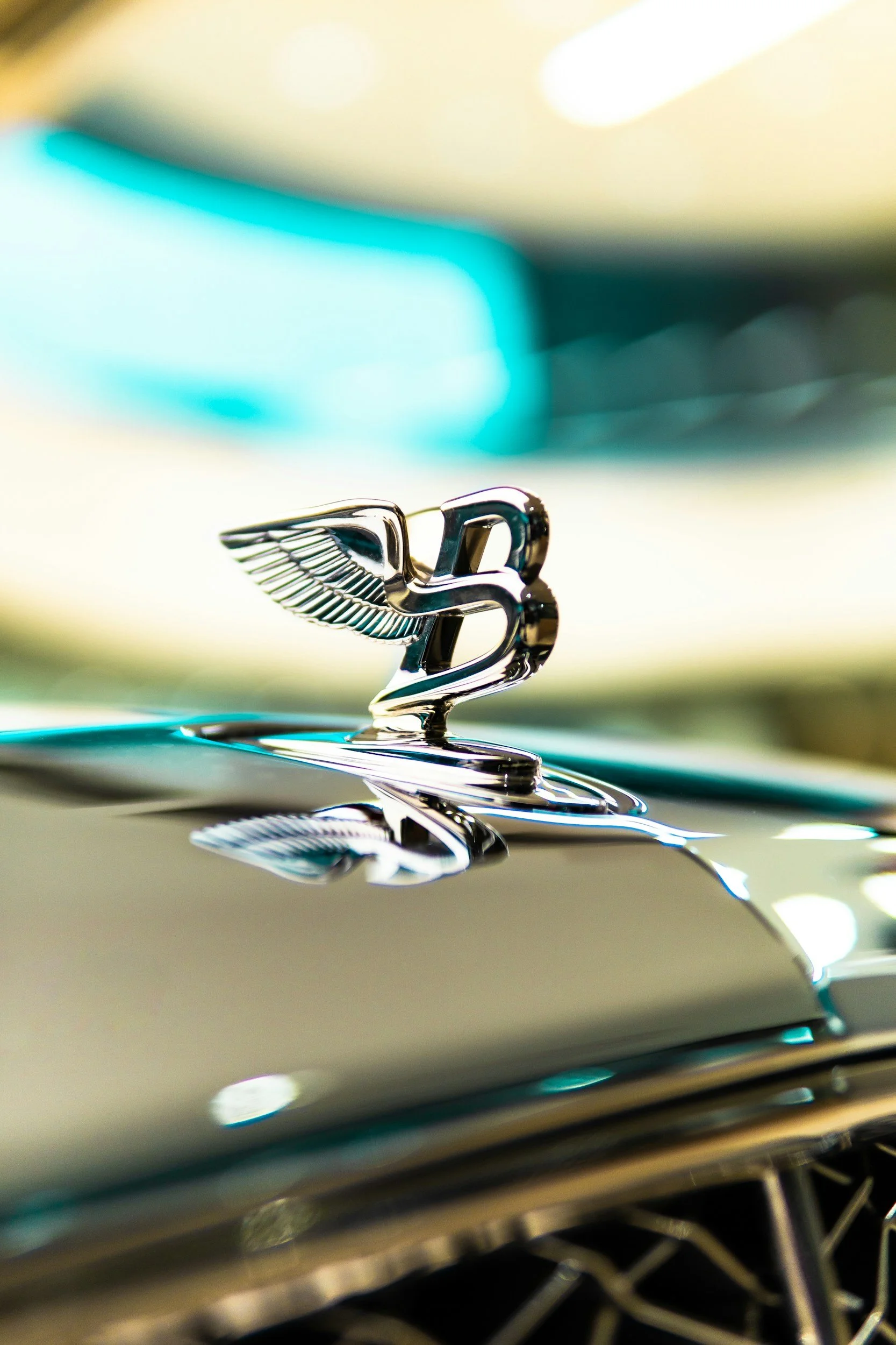 A shiny chrome vintage car hood ornament featuring a winged figure, reflecting surrounding lights.