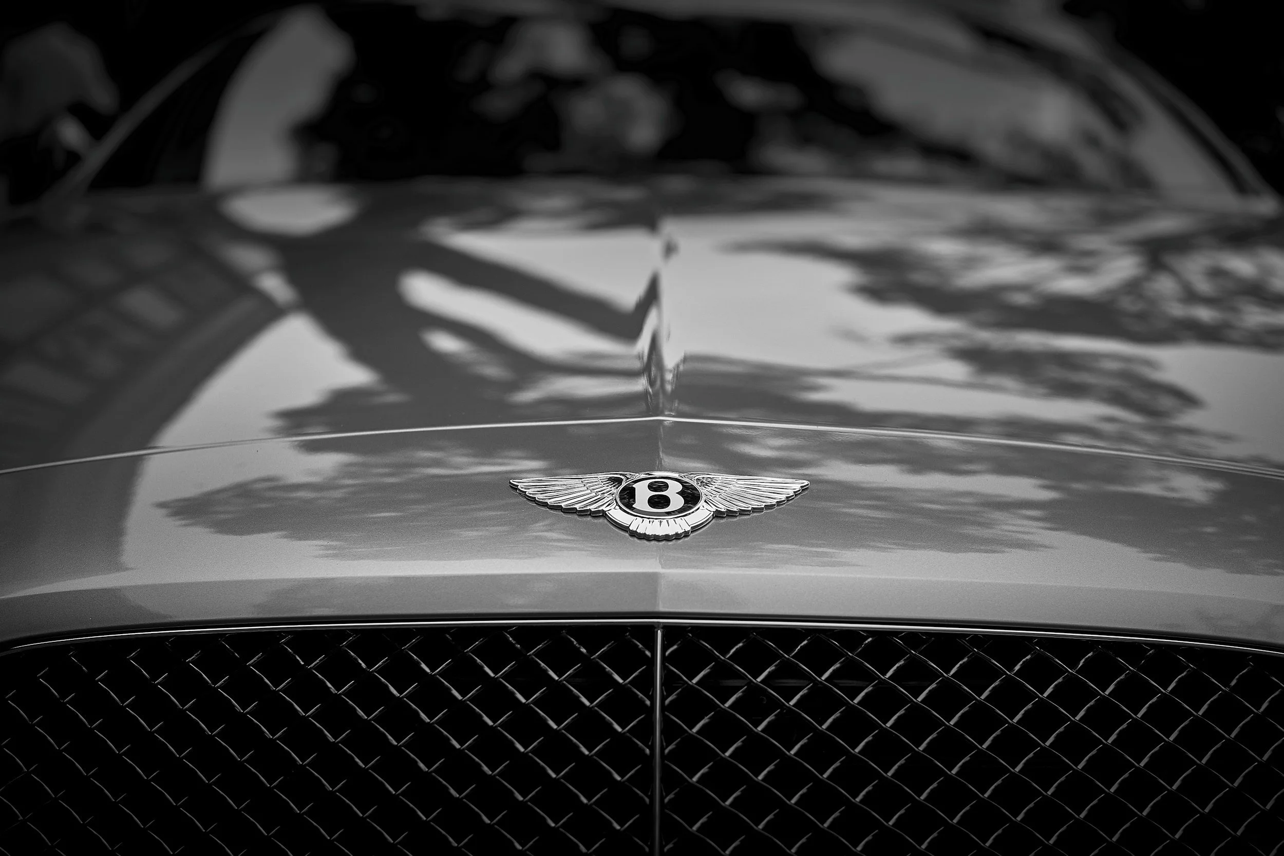 Close-up of the front of a luxury Bentley car with the brand's emblem on the hood, black and white photograph.
