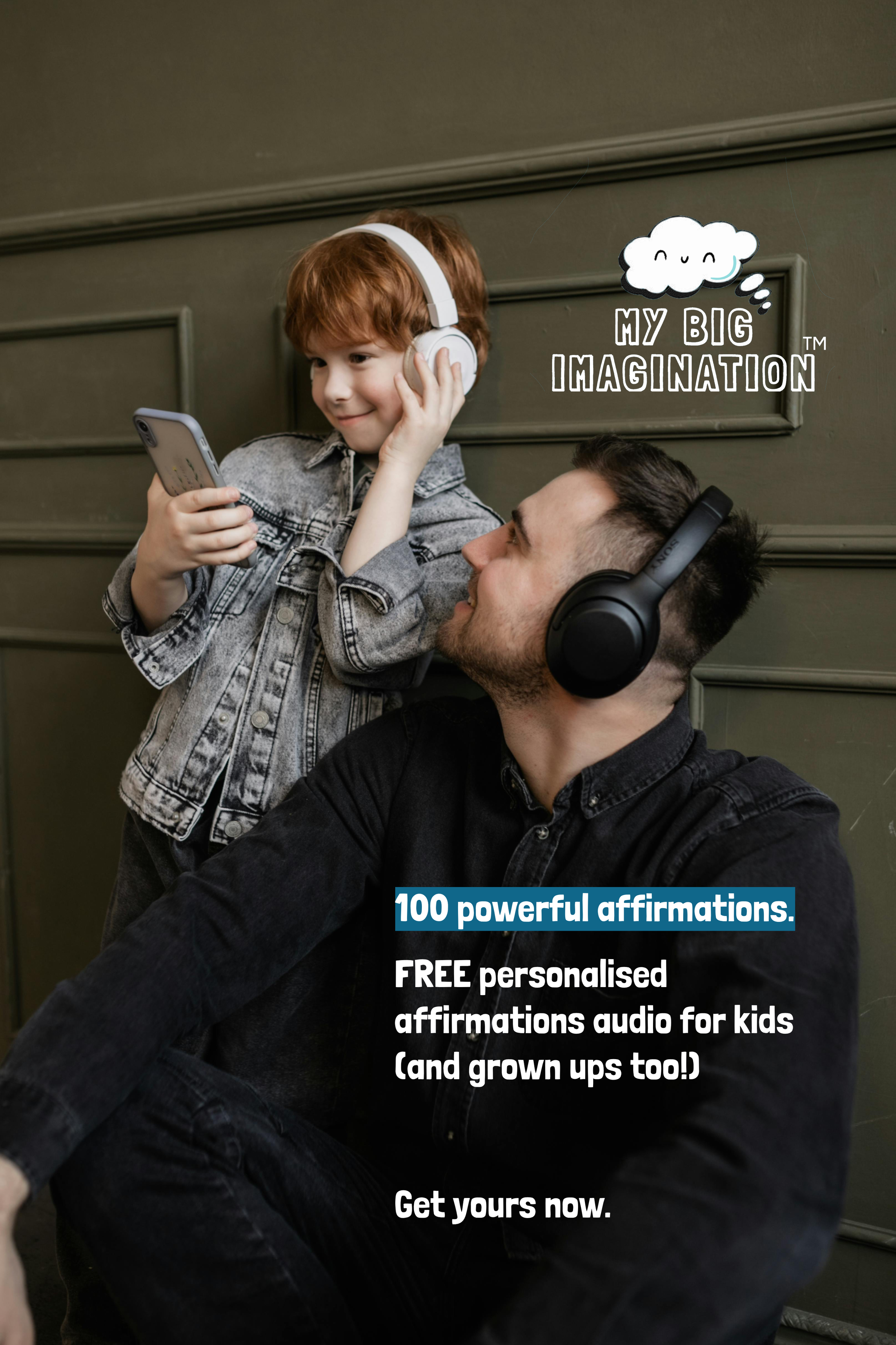 A young boy with red hair wearing white headphones and holding a smartphone, talking to a man with dark hair wearing black headphones, sitting against a green wall.