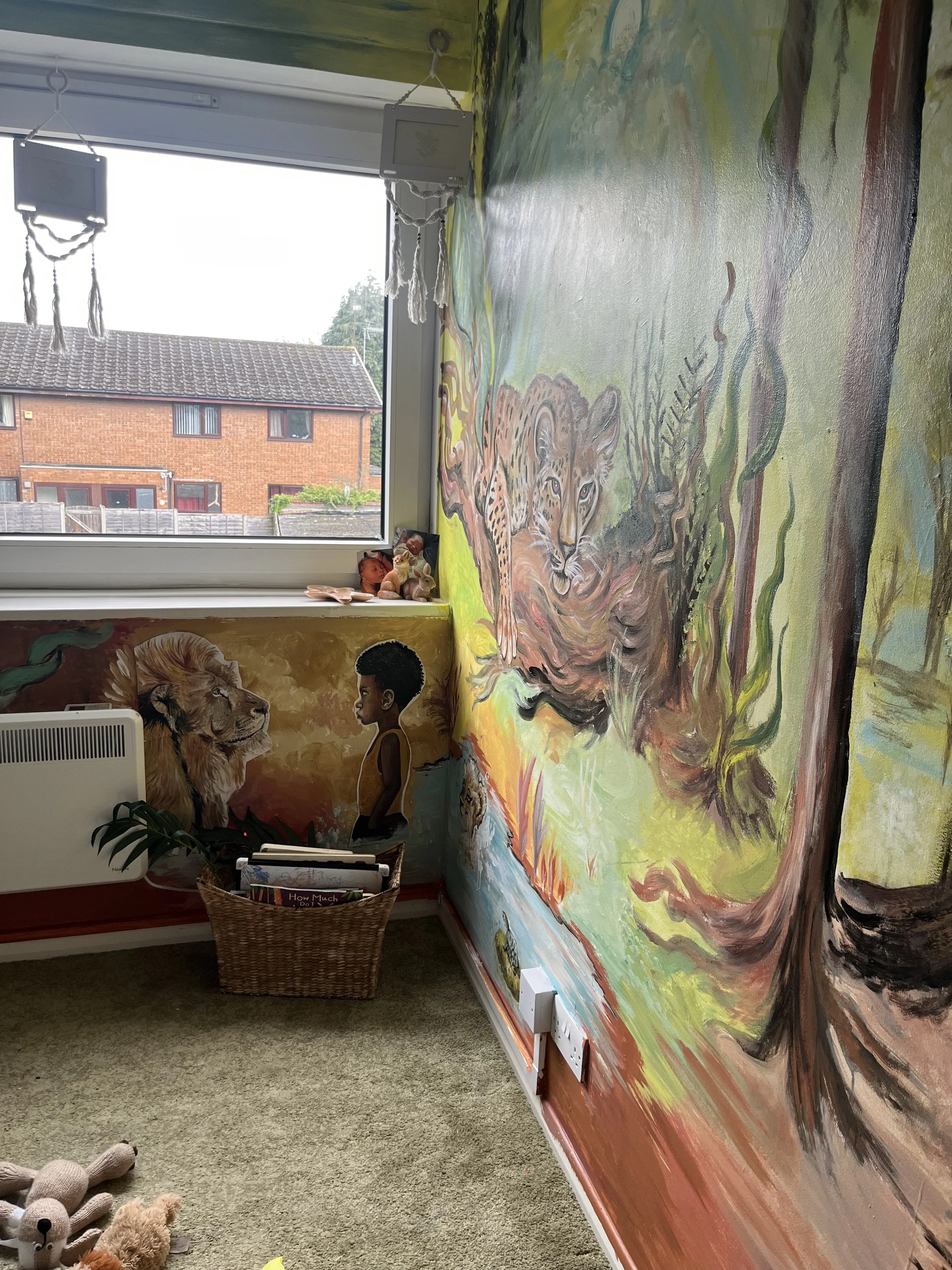 Colorful jungle-themed mural featuring a lion and a boy on a wall in a room with a window and children's toys.