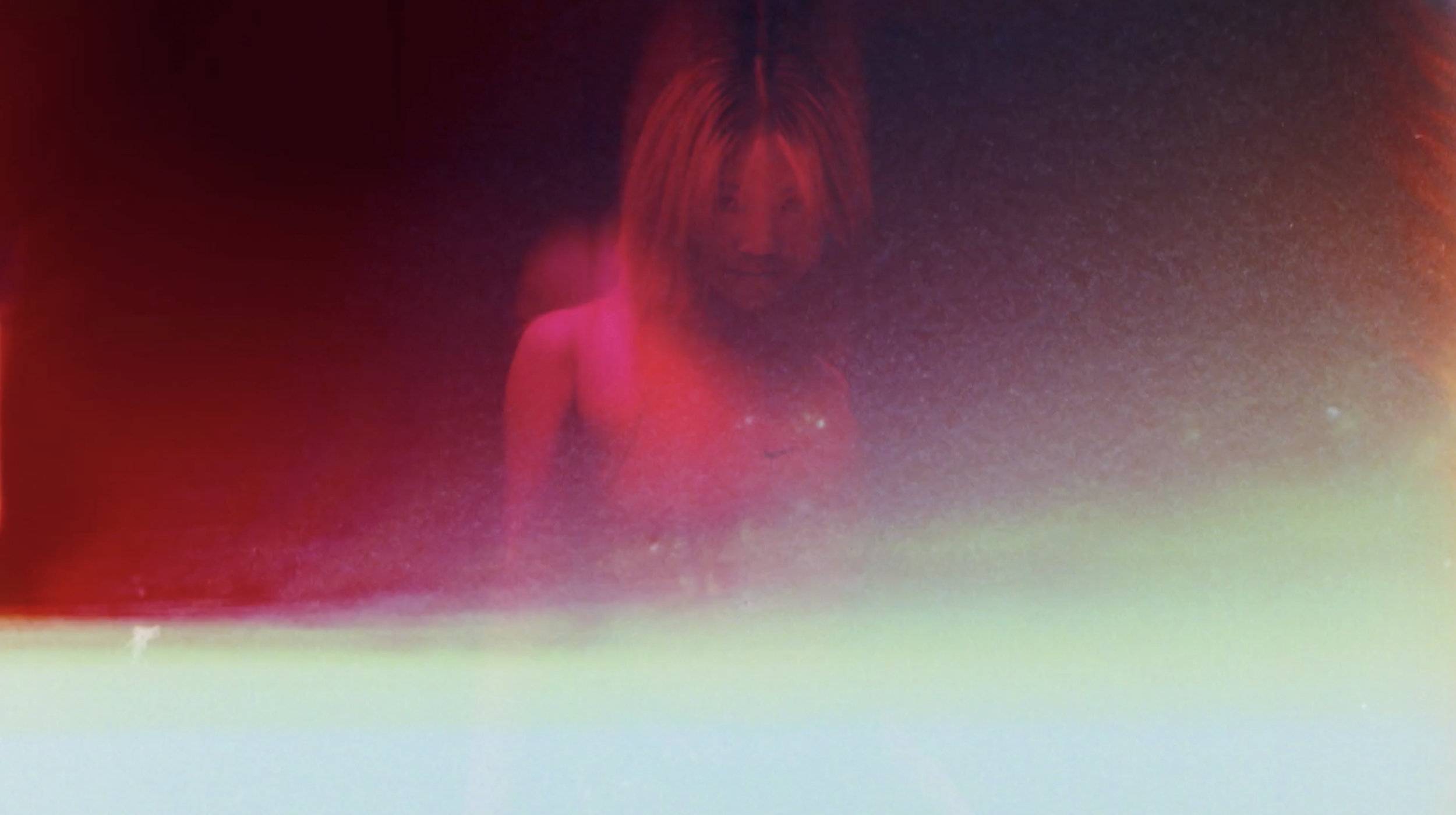 A woman with long blonde hair looking at a screen with a gradient colorful reflection.