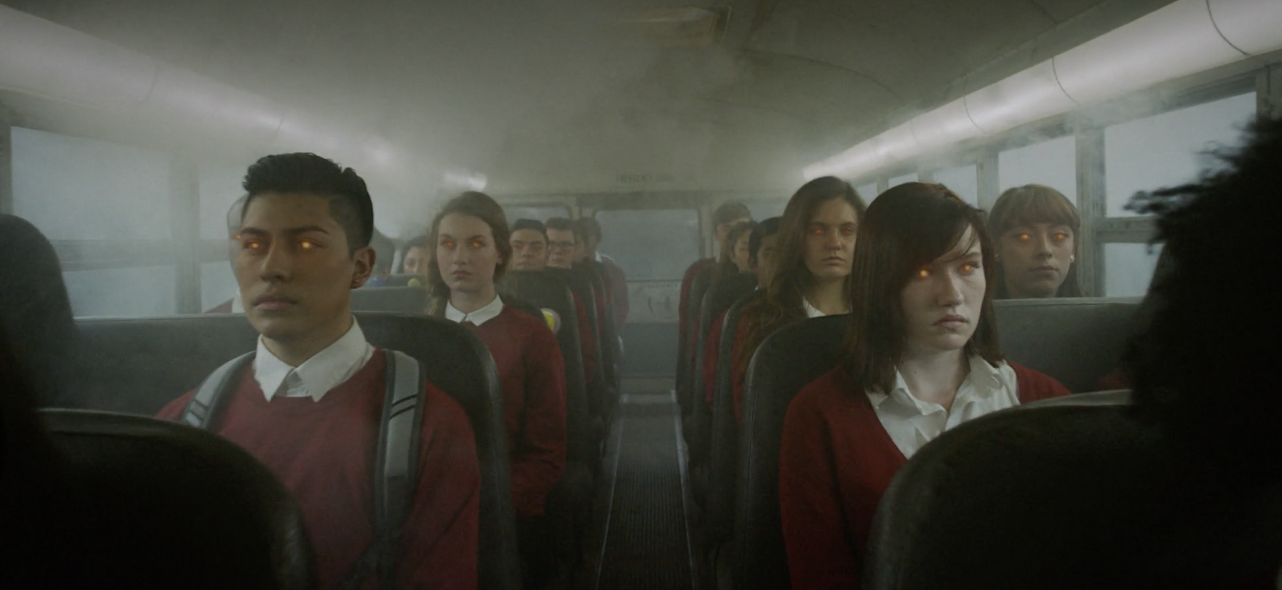 Scene inside a school bus with students having glowing eyes, wearing school uniforms including white shirts and red sweaters, sitting in rows facing forward.