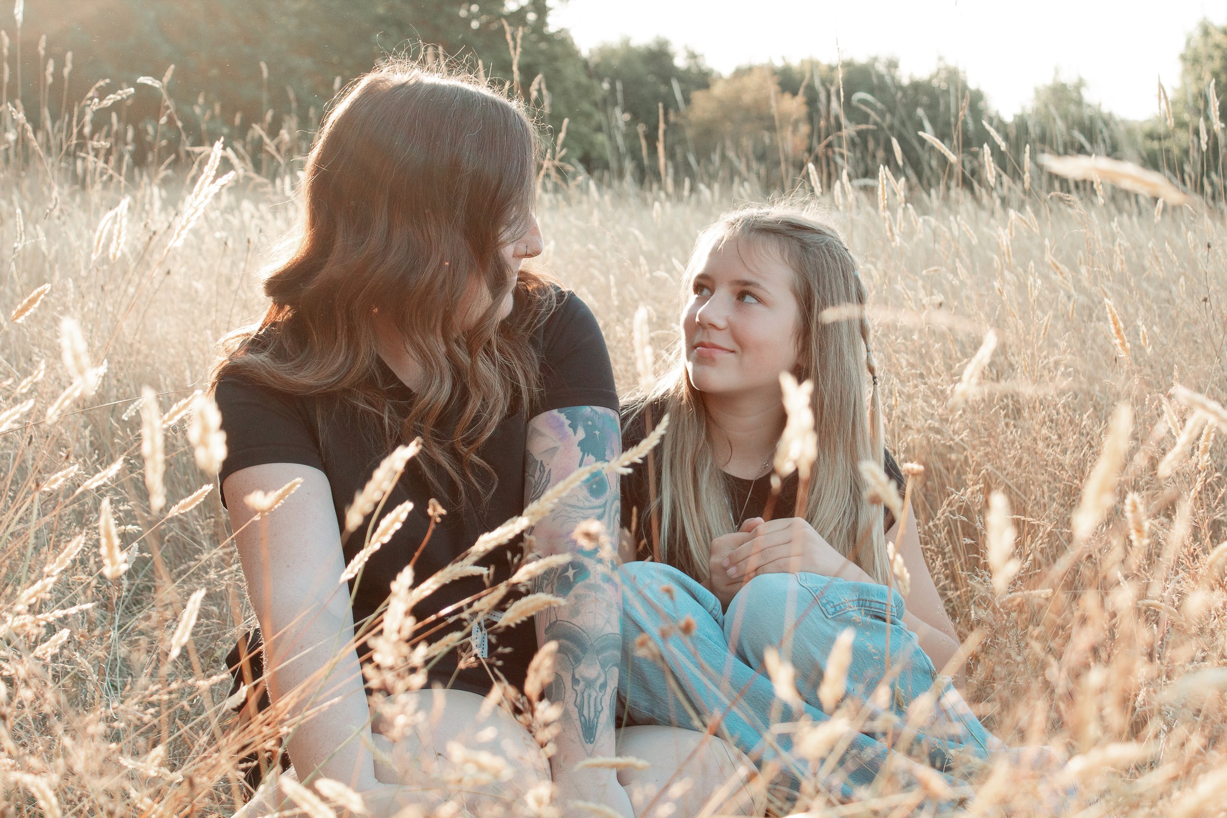 A woman and a girl sitting in a field of tall, dry grass, looking at each other.