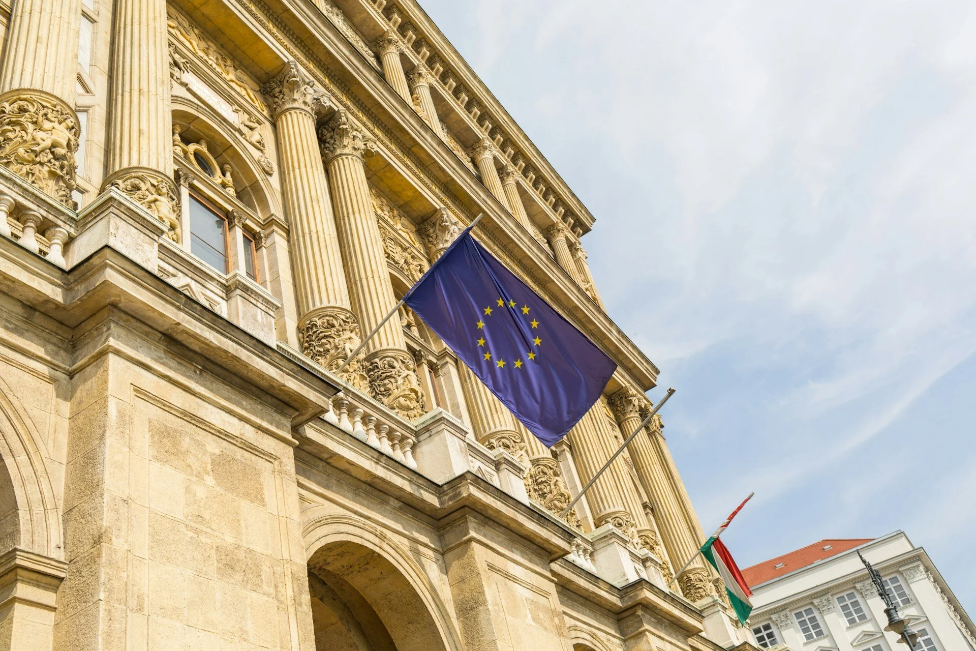 European Union flag flying outside a historic building in Brussels, EU regulatory policy and public policy and government affairs.
