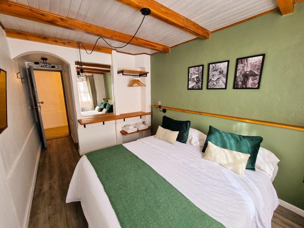 Habitación con cama grande, paredes verdes, decoración en tonos neutros, madera en el techo y detalles decorativos en blanco y verde.