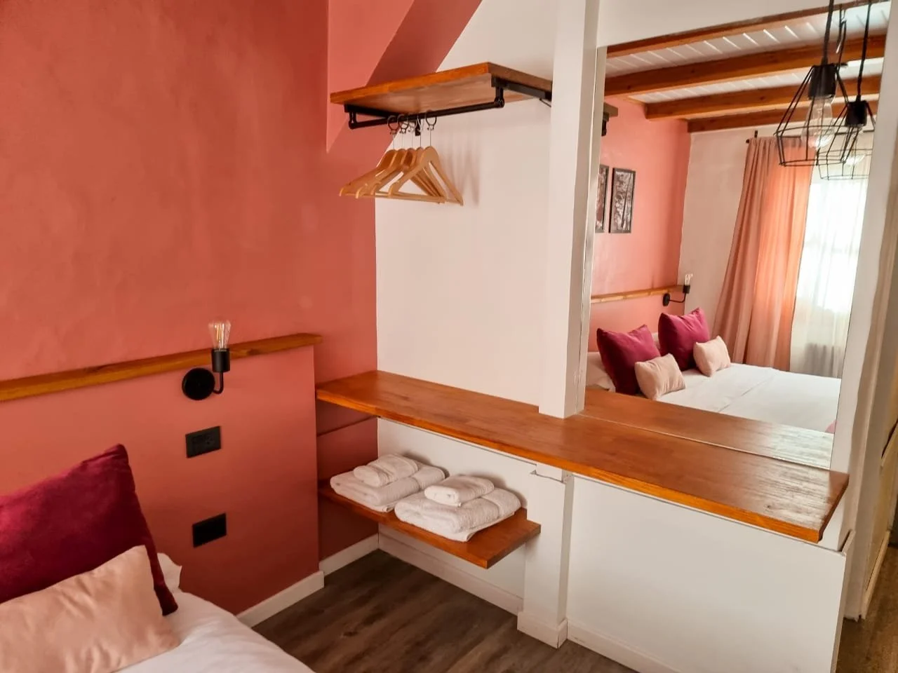 Habitación decorada con paredes en color rosa, cama con almohadas rosas y beige, cortinas rosadas, muebles de madera y una lámpara de pared.