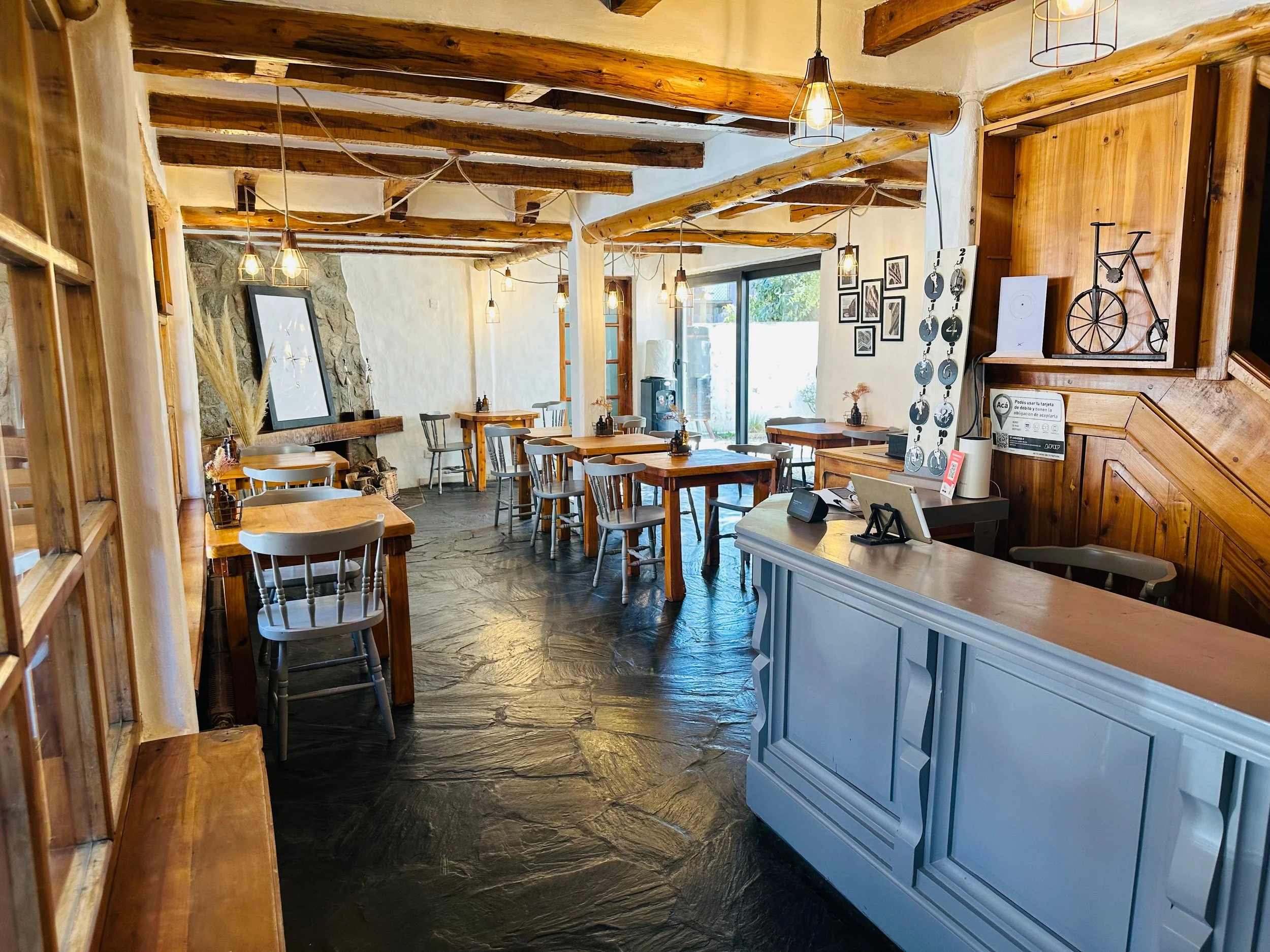 Interior de un restaurante con mesas de madera, paredes blancas, vigas de madera en el techo y decoración moderna con cuadros y una bicicleta de decoración.
