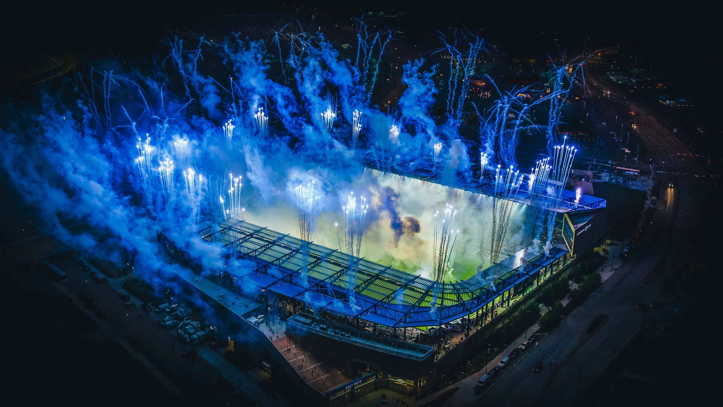 Aerial view of a football stadium at night with fireworks exploding above during a celebration or event.