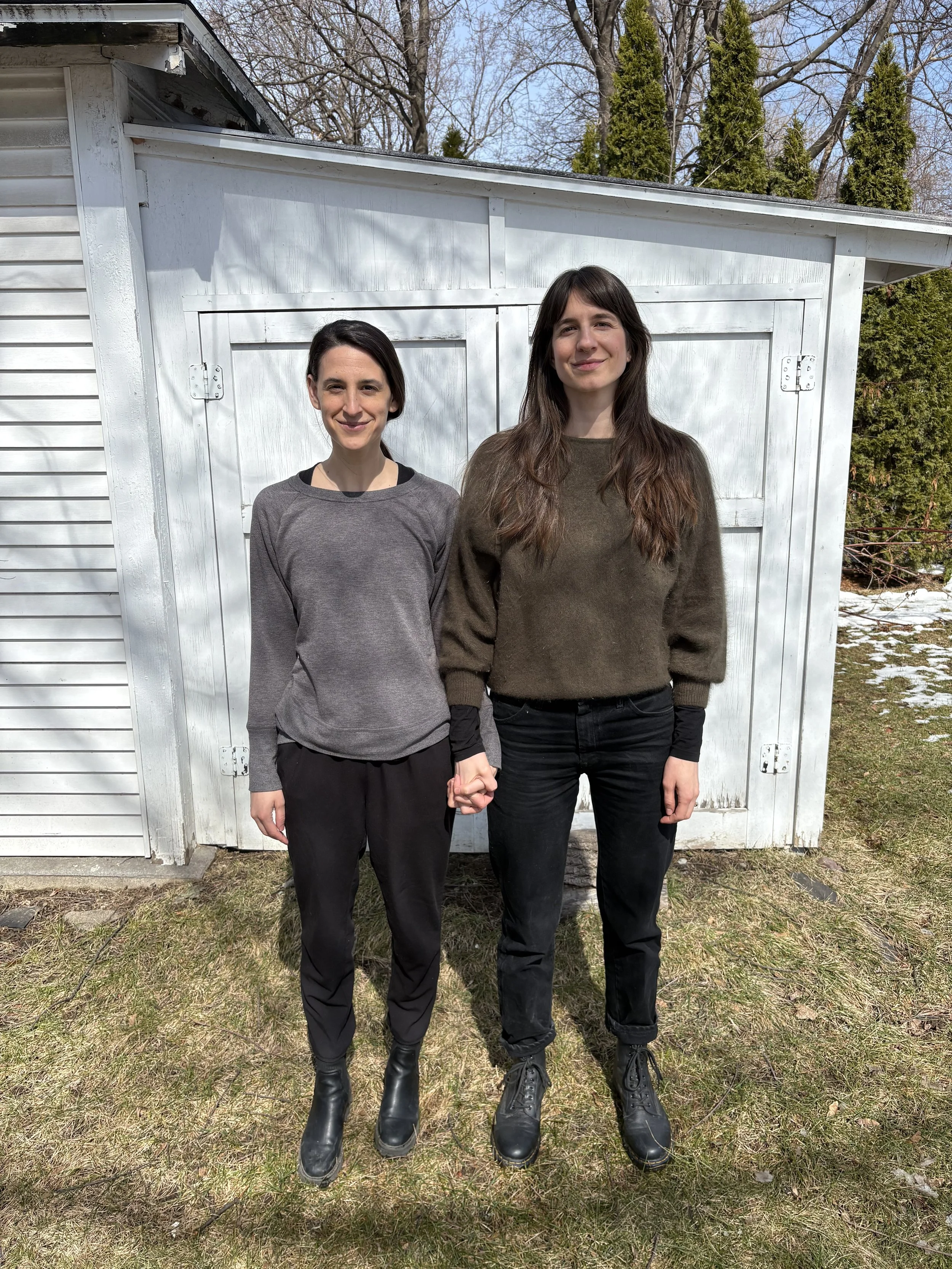 Two women stand side by side holding hands.