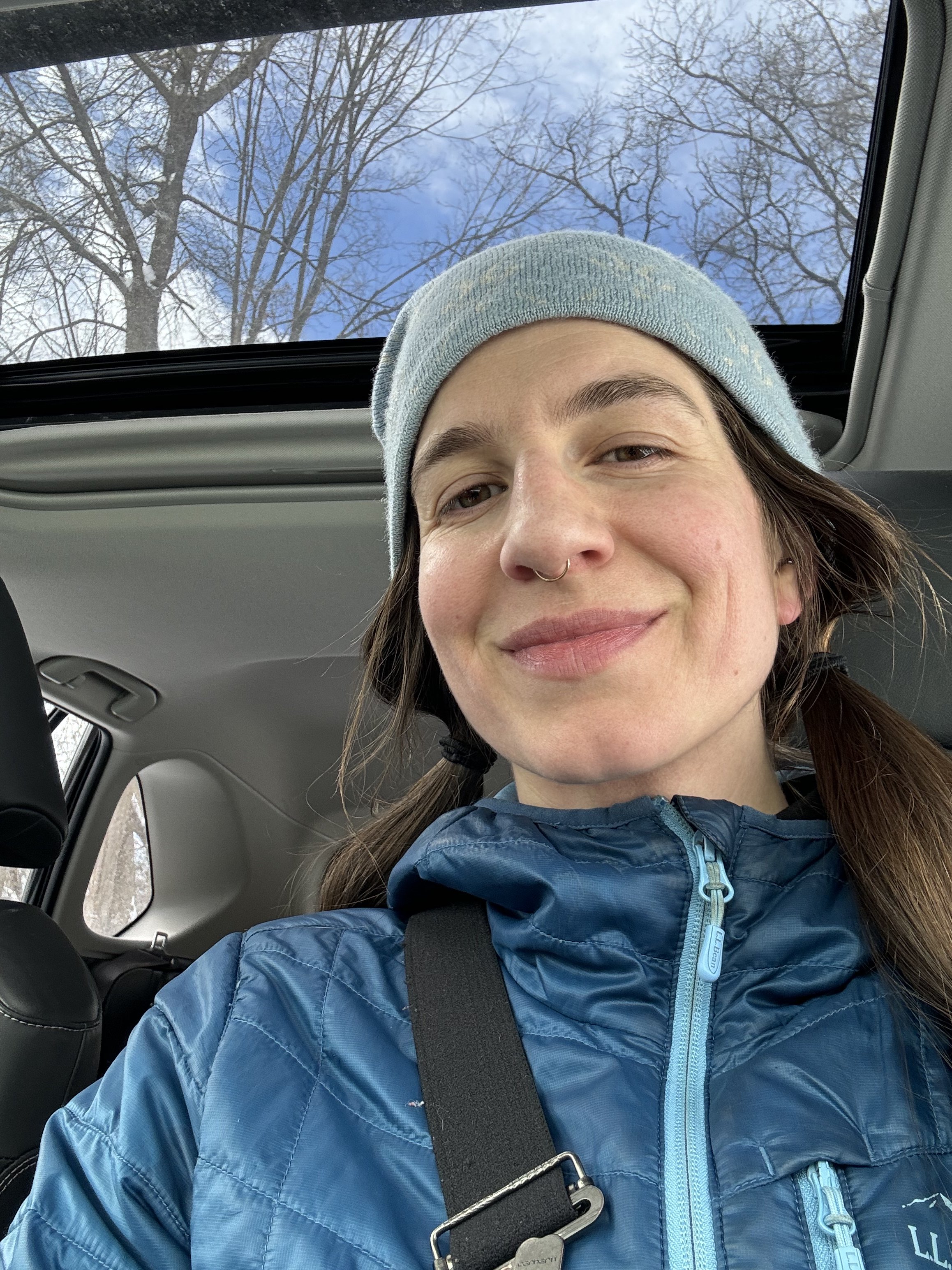 A woman, seated in her car, smiling at the camera