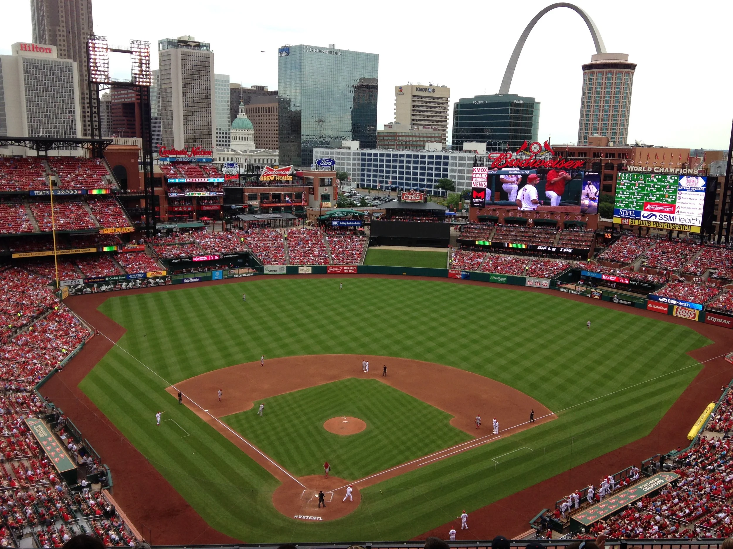 The view from behind home plate, high in the stands at a St. Louis Cardinals baseball game. The St. Louis skyline, including The Arch, can be seen in the background.