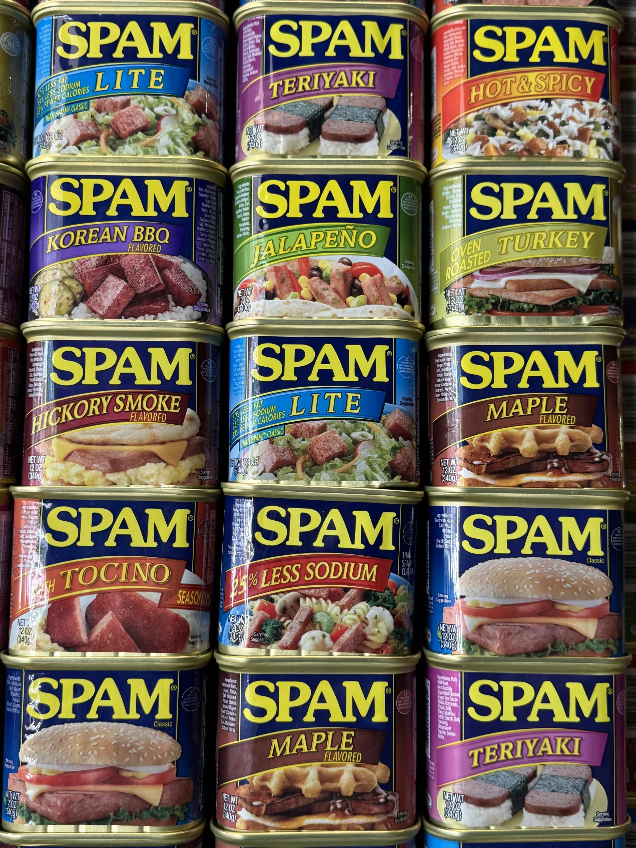 Close-up of nine cans of Spam in different varieties arranged together.